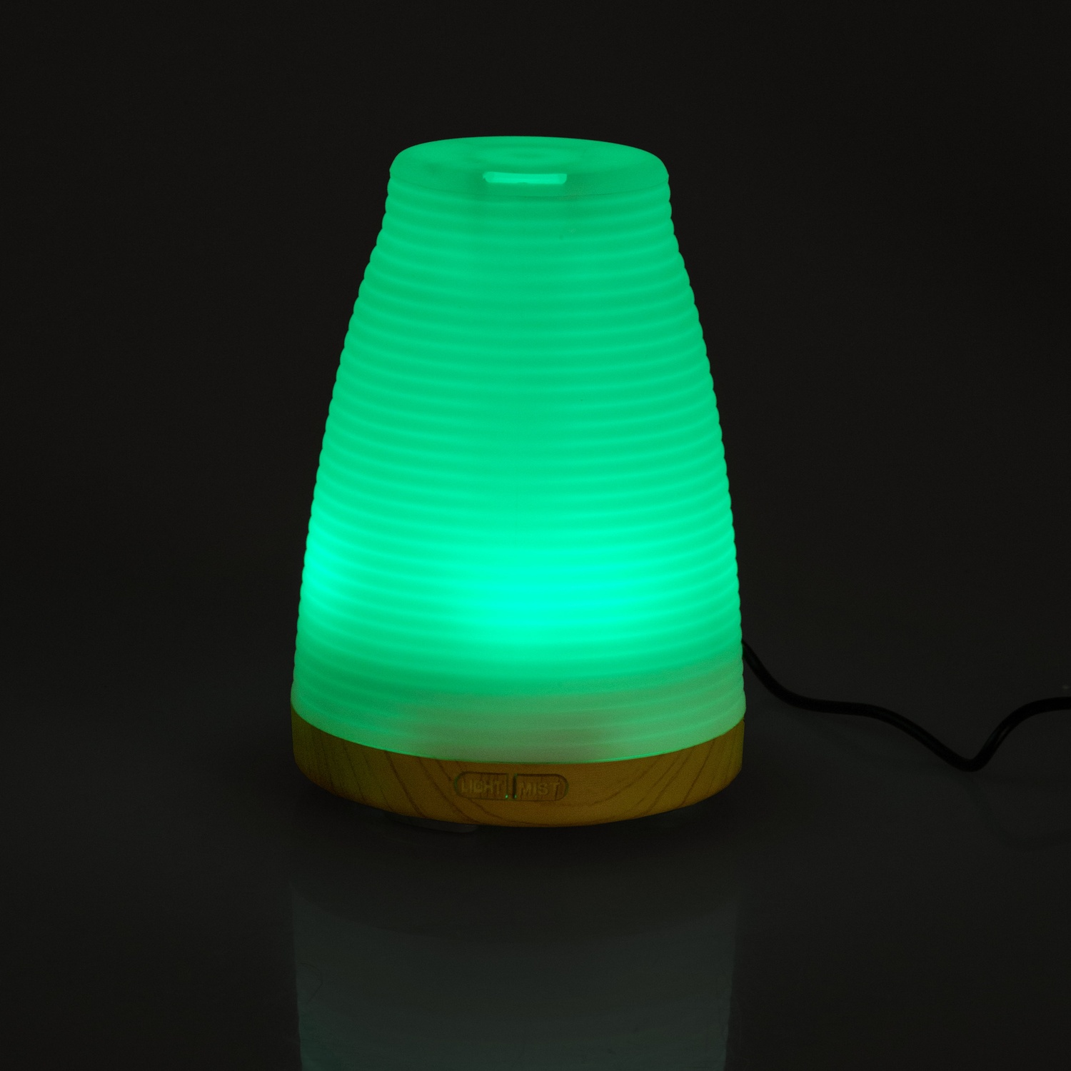 Luce verde all'interno di un piccolo diffusore bianco e scanalato con una base marrone chiaro.