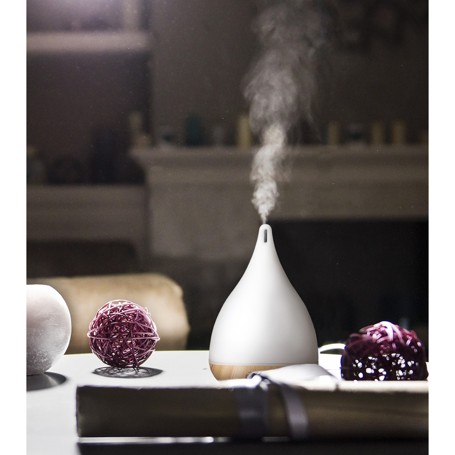 Diffusore di oli essenziali bianco con vapore, palline decorative viola e candela.