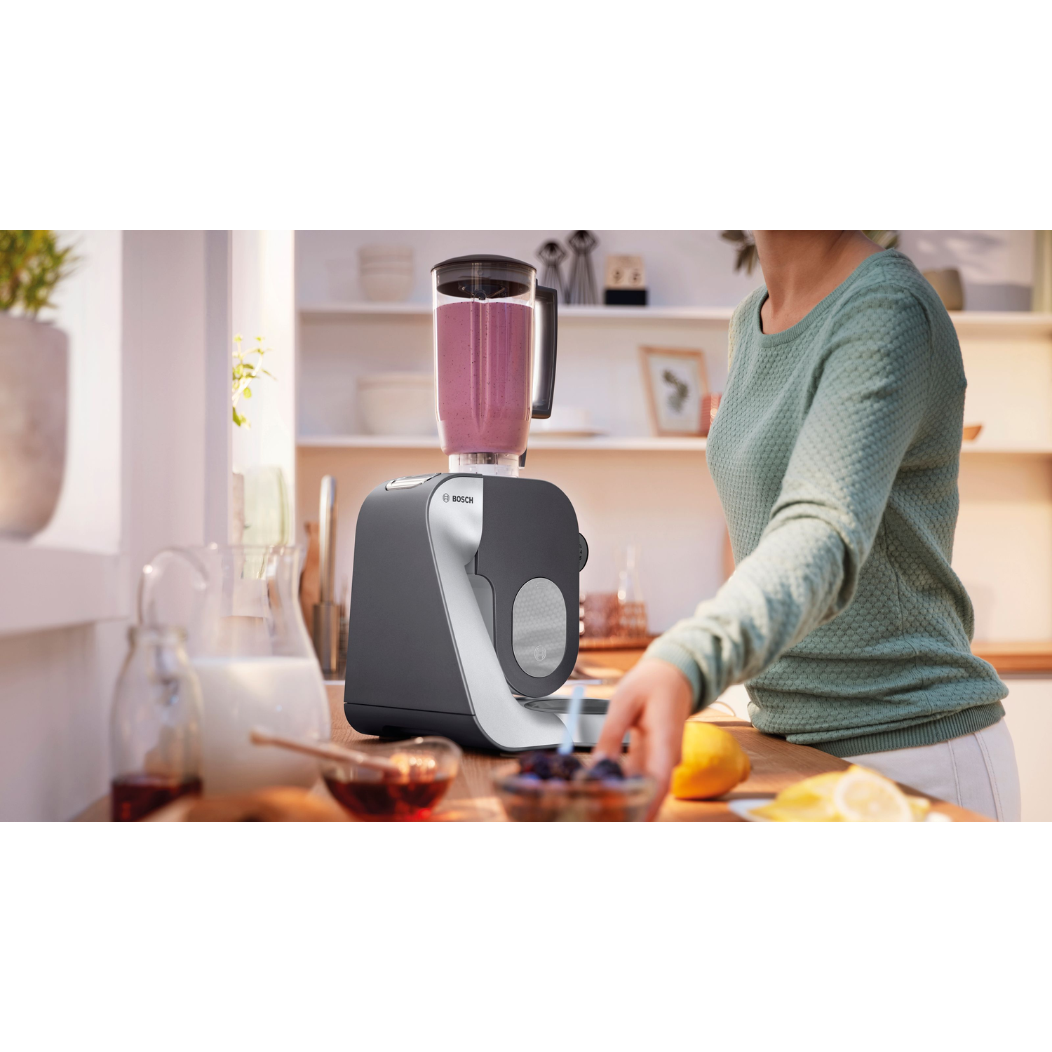 Une femme utilise un blender Bosch dans une cuisine avec du lait, du miel et un citron sur le comptoir.
