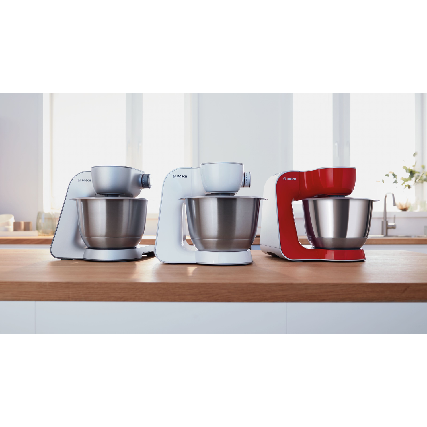 Trois robots pâtissiers en blanc, argent et rouge sur une surface en bois.