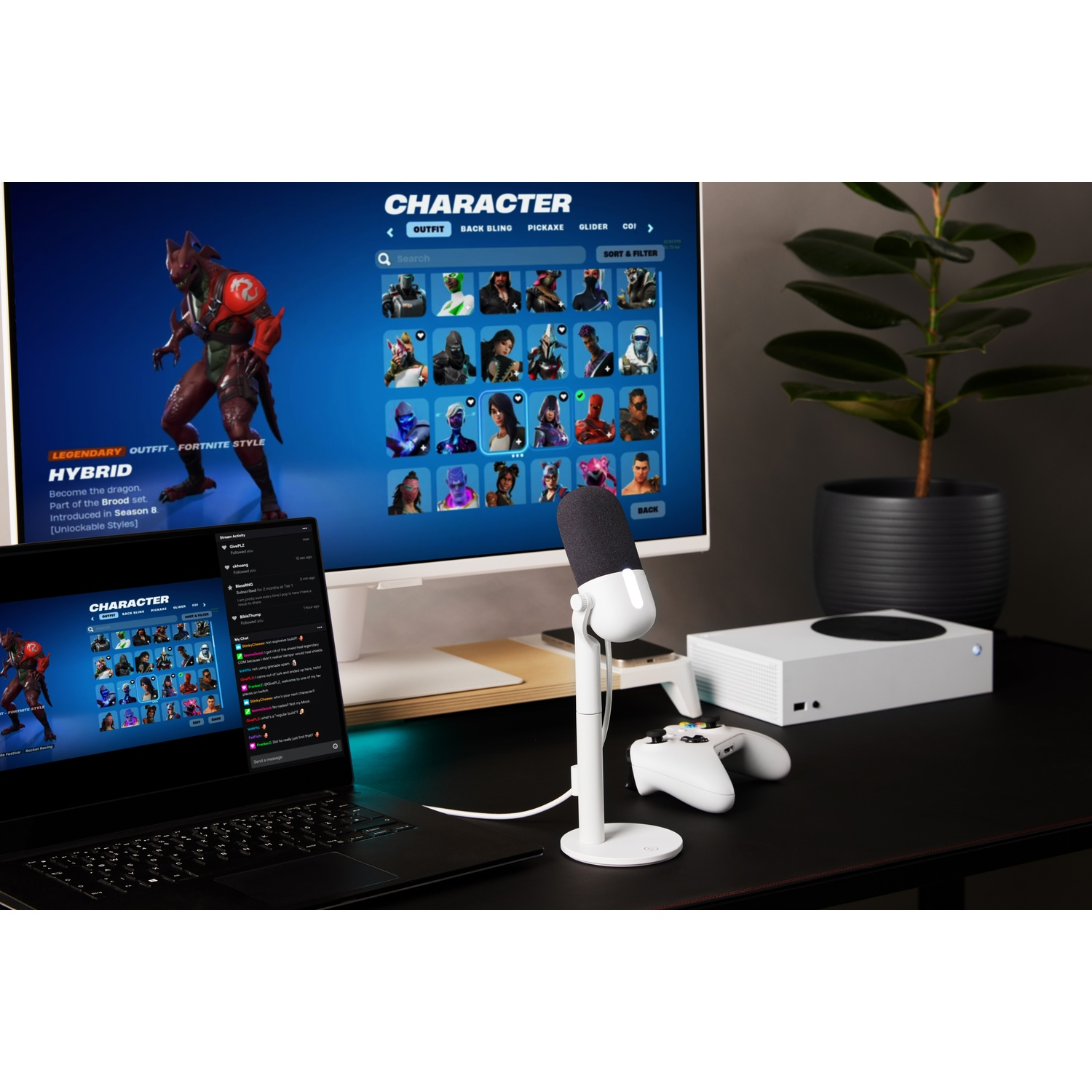 A gaming setup with a laptop, monitor showing a game screen, a microphone, and a white game console.