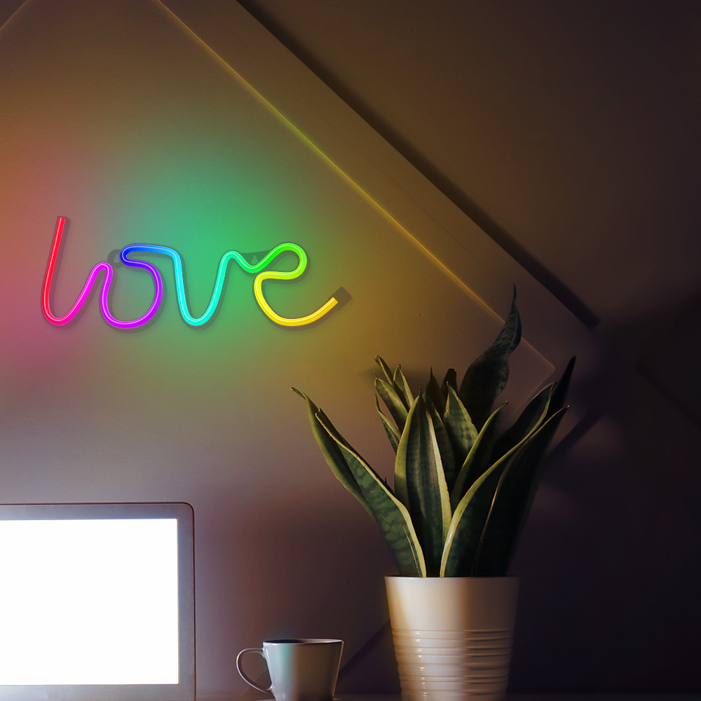 Egy neonfelirat, amely a 'love' szót jeleníti meg egy növény és egy csésze felett.