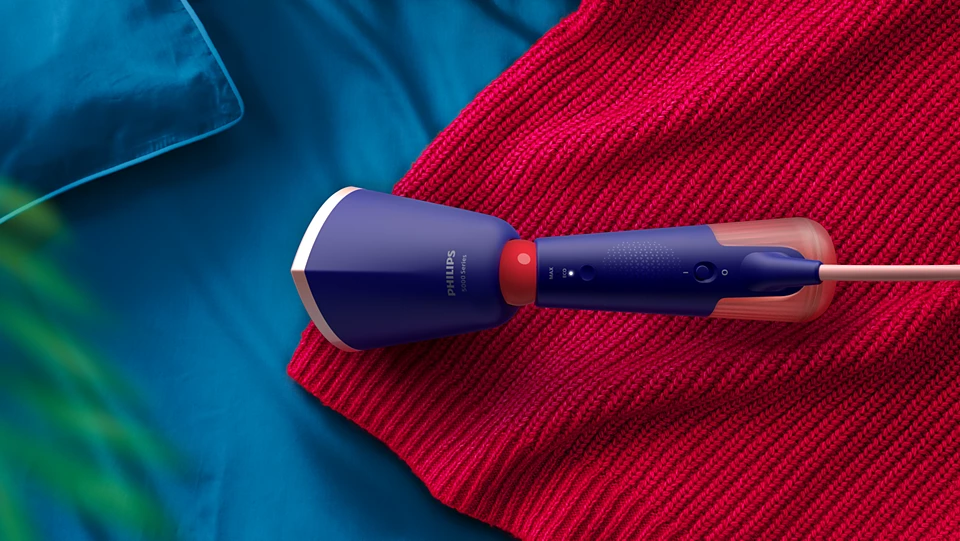 Ein blauer Philips-Dampfgarer auf einem roten Strickstoff, mit einem blauen Kissen im Hintergrund.