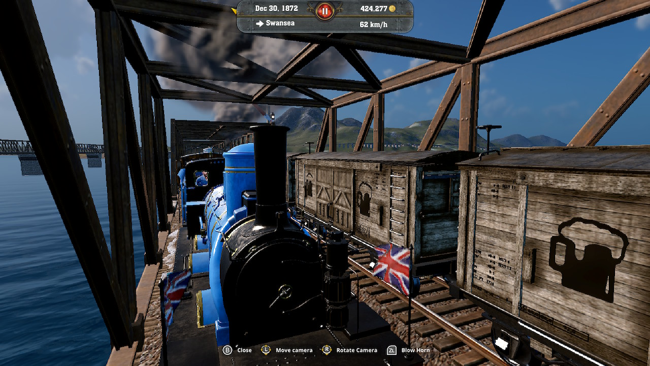 Train bleu sur un pont au-dessus de l'eau, avec un drapeau Union Jack et un panneau de bière.
