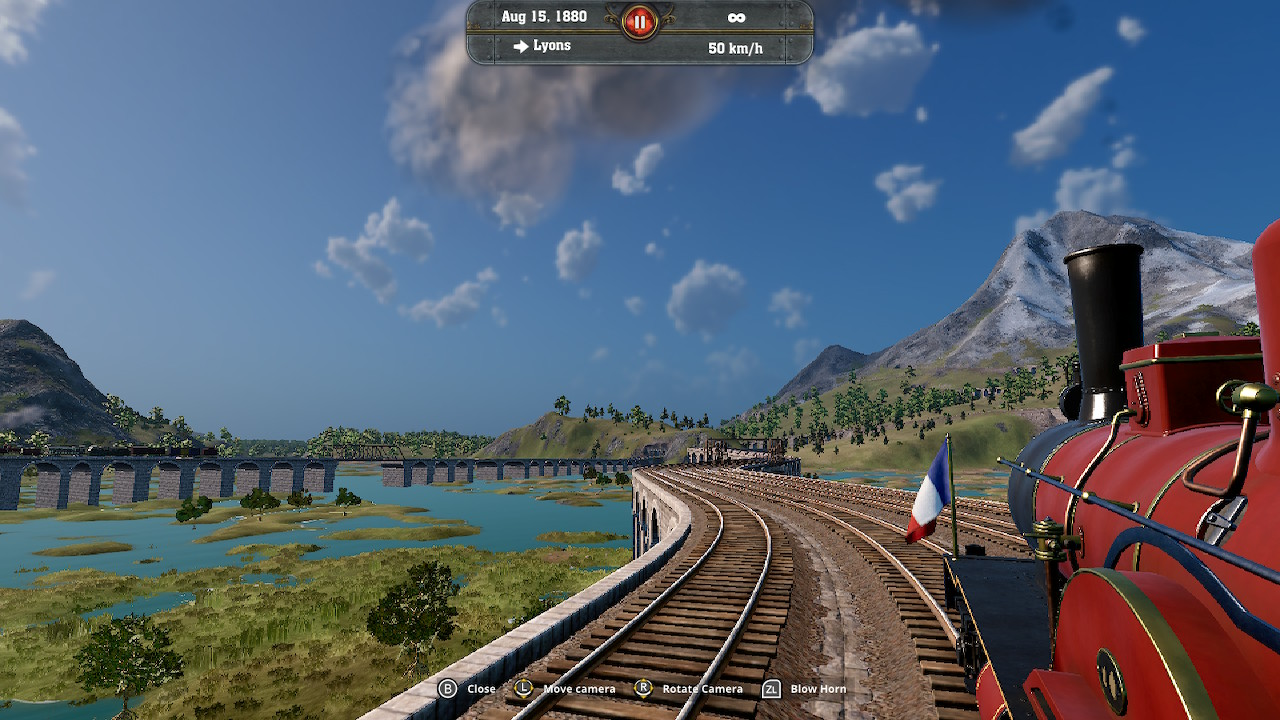 Un train rouge sur des rails dans un paysage avec un pont et des montagnes.