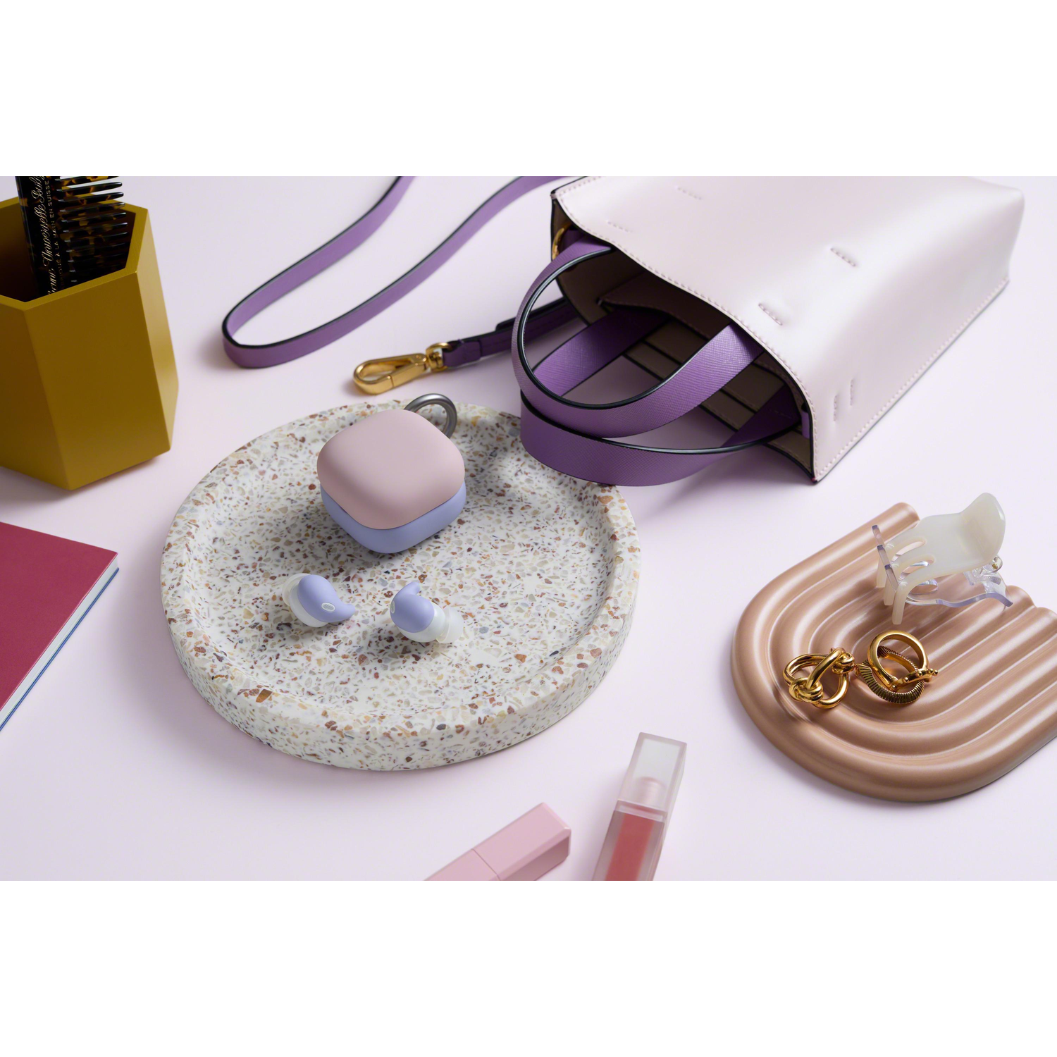 Oordopjes, accessoires en een tas op een roze oppervlak.