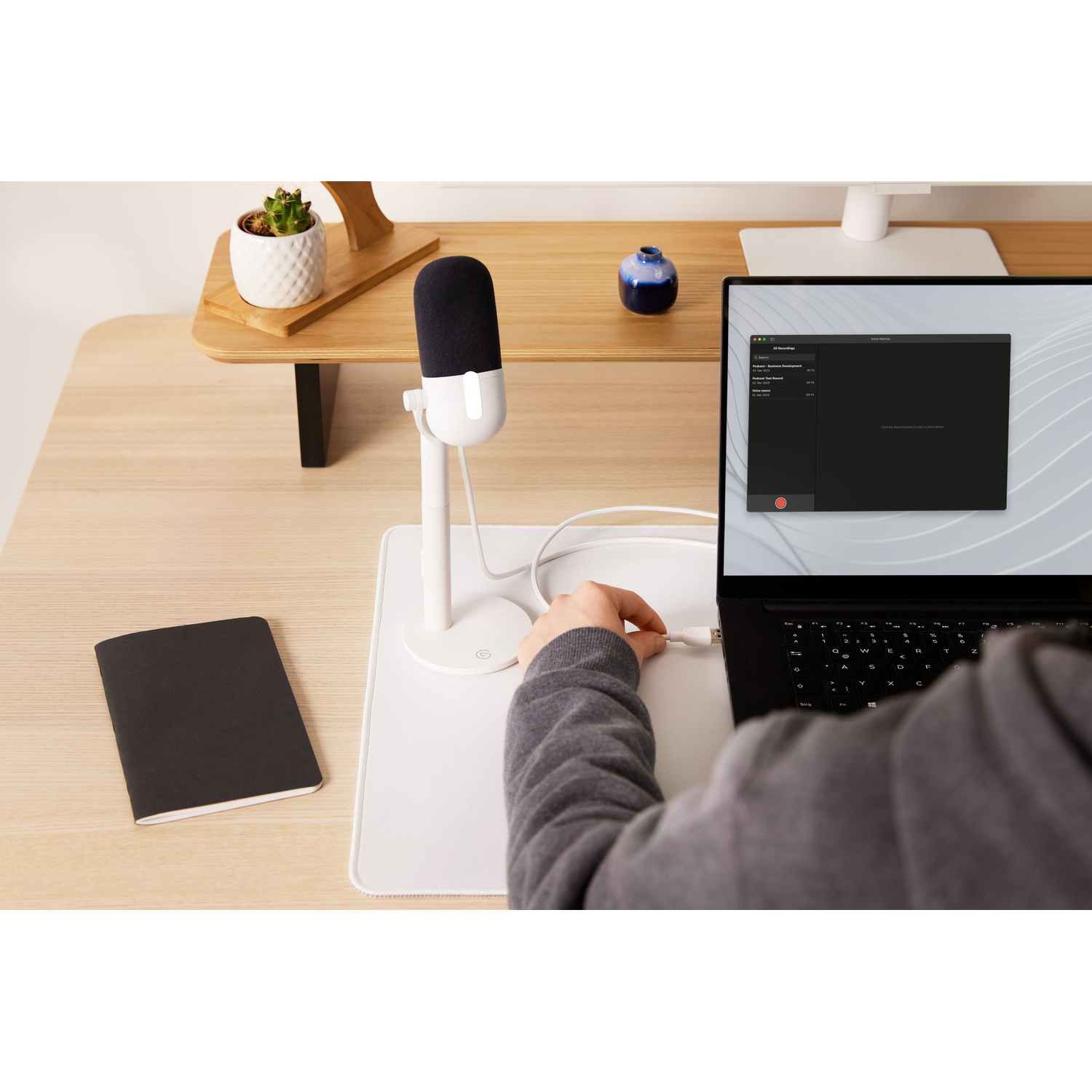 Person using a laptop with a microphone and notebook on a desk.