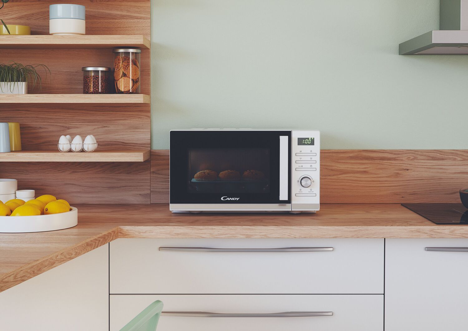 Un horno microondas blanco sobre una encimera de madera en una cocina con una pared verde claro y estantes de madera.