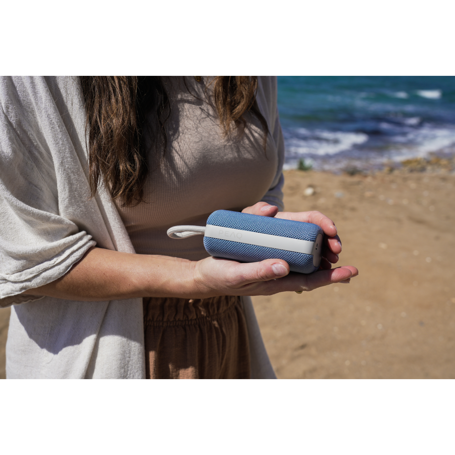 Vrouw die een blauwe speaker op het strand vasthoudt.