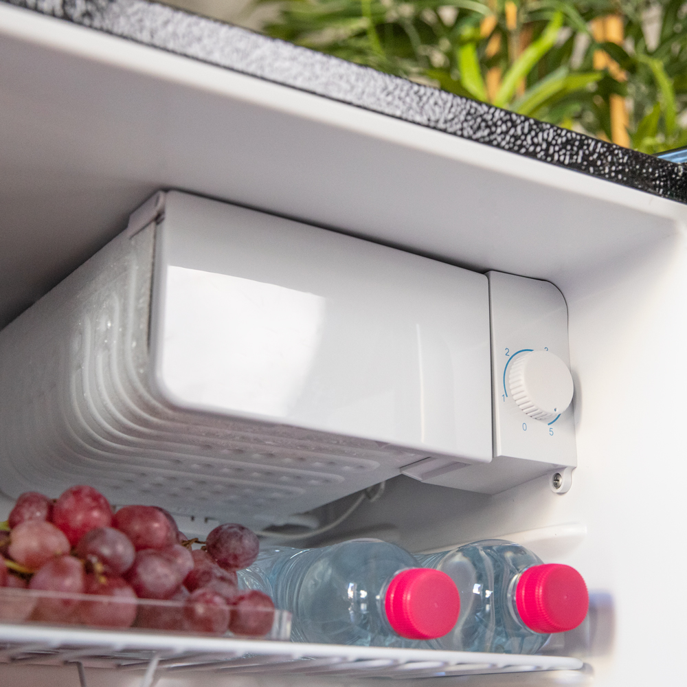 Refrigerador abierto con uvas y botellas de agua. Interior blanco con un dial de control.
