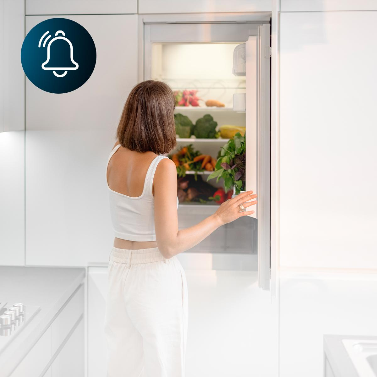 Mujer abriendo un refrigerador en una cocina moderna, con un icono de campana.