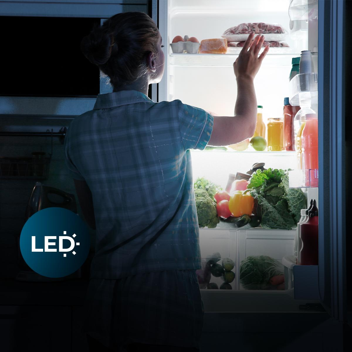 Mujer con camisa a cuadros azules alcanzando dentro de un refrigerador iluminado por LED.