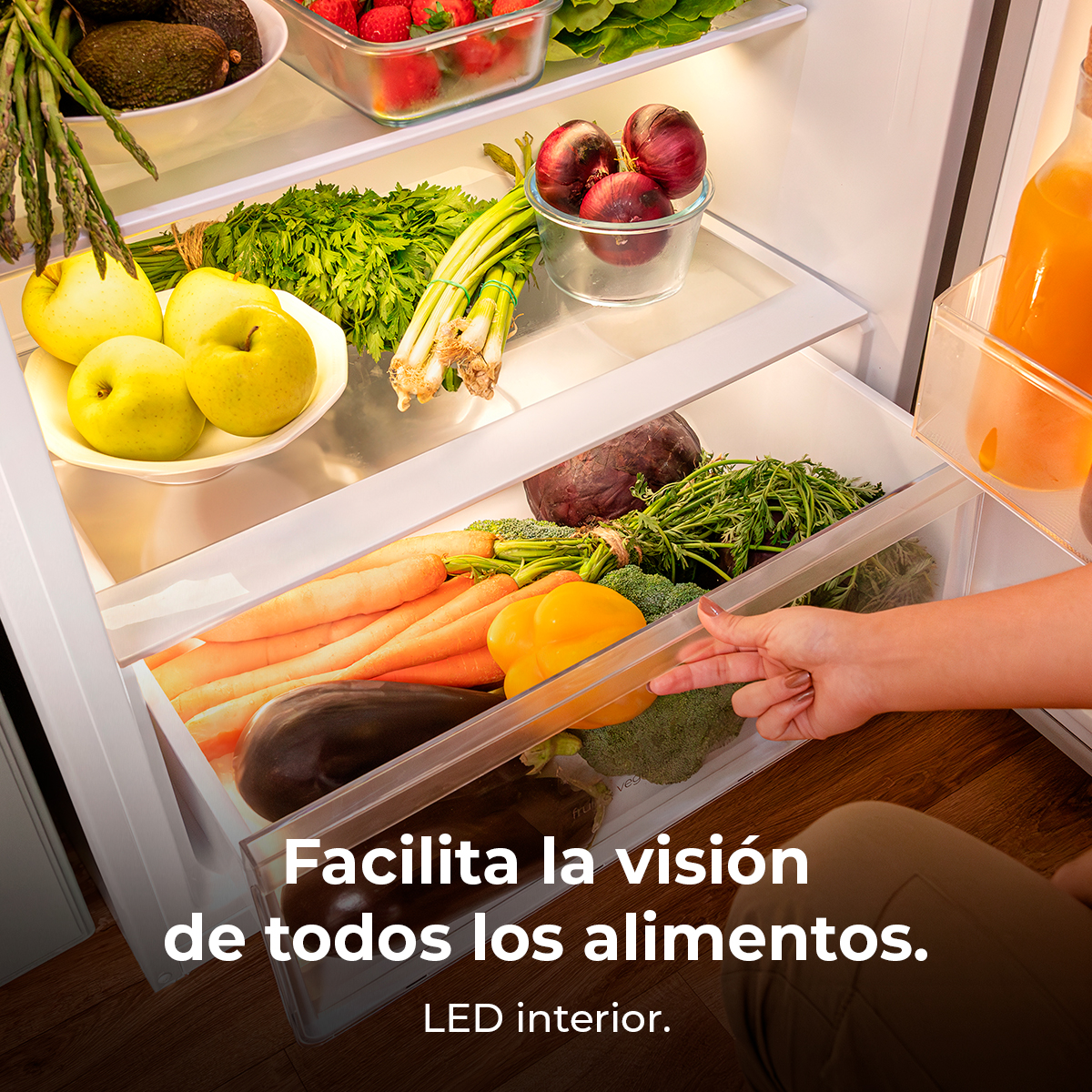 La mano de una mujer abriendo un cajón de refrigerador lleno de comida.