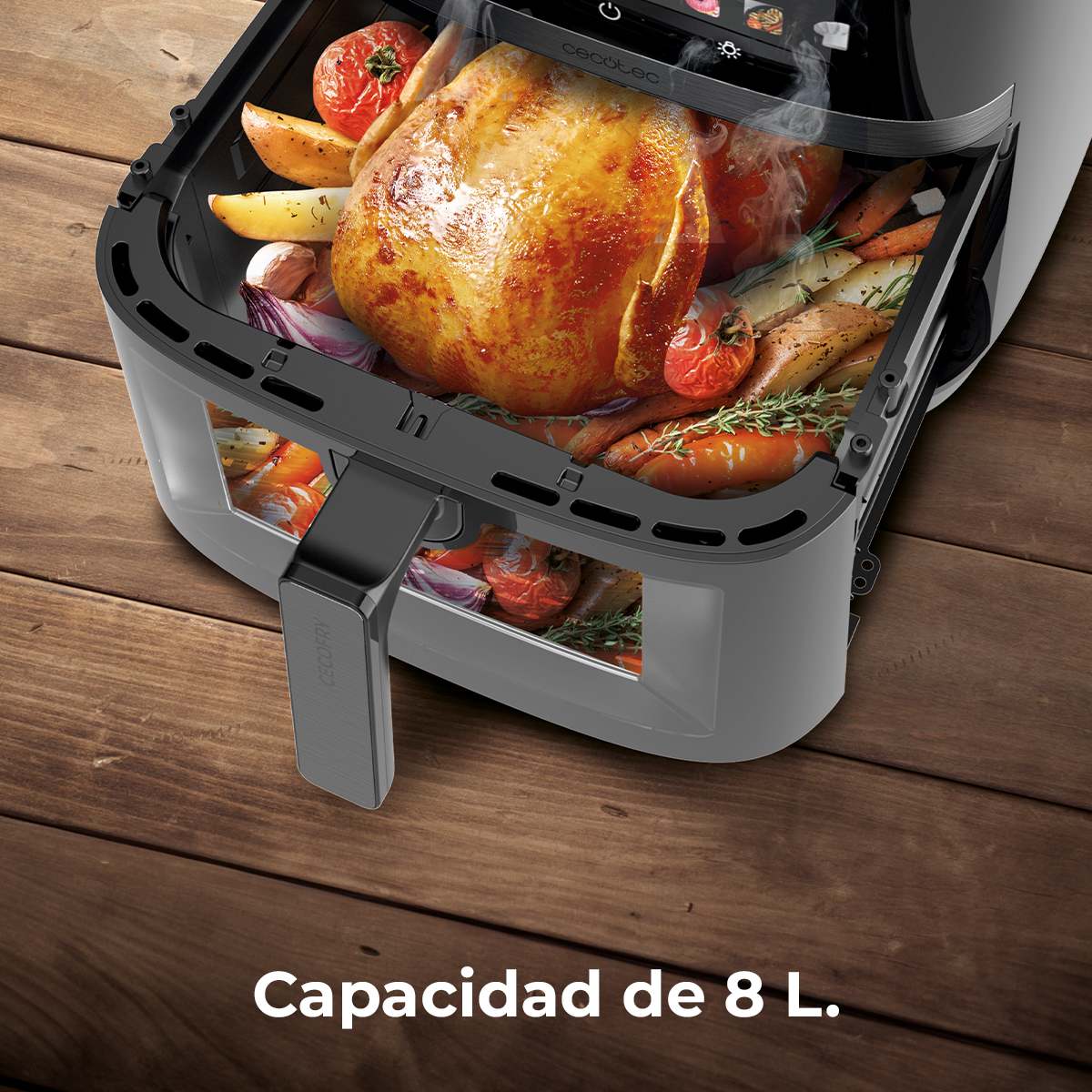 Una freidora de aire con pollo asado y verduras dentro, sobre una mesa de madera.