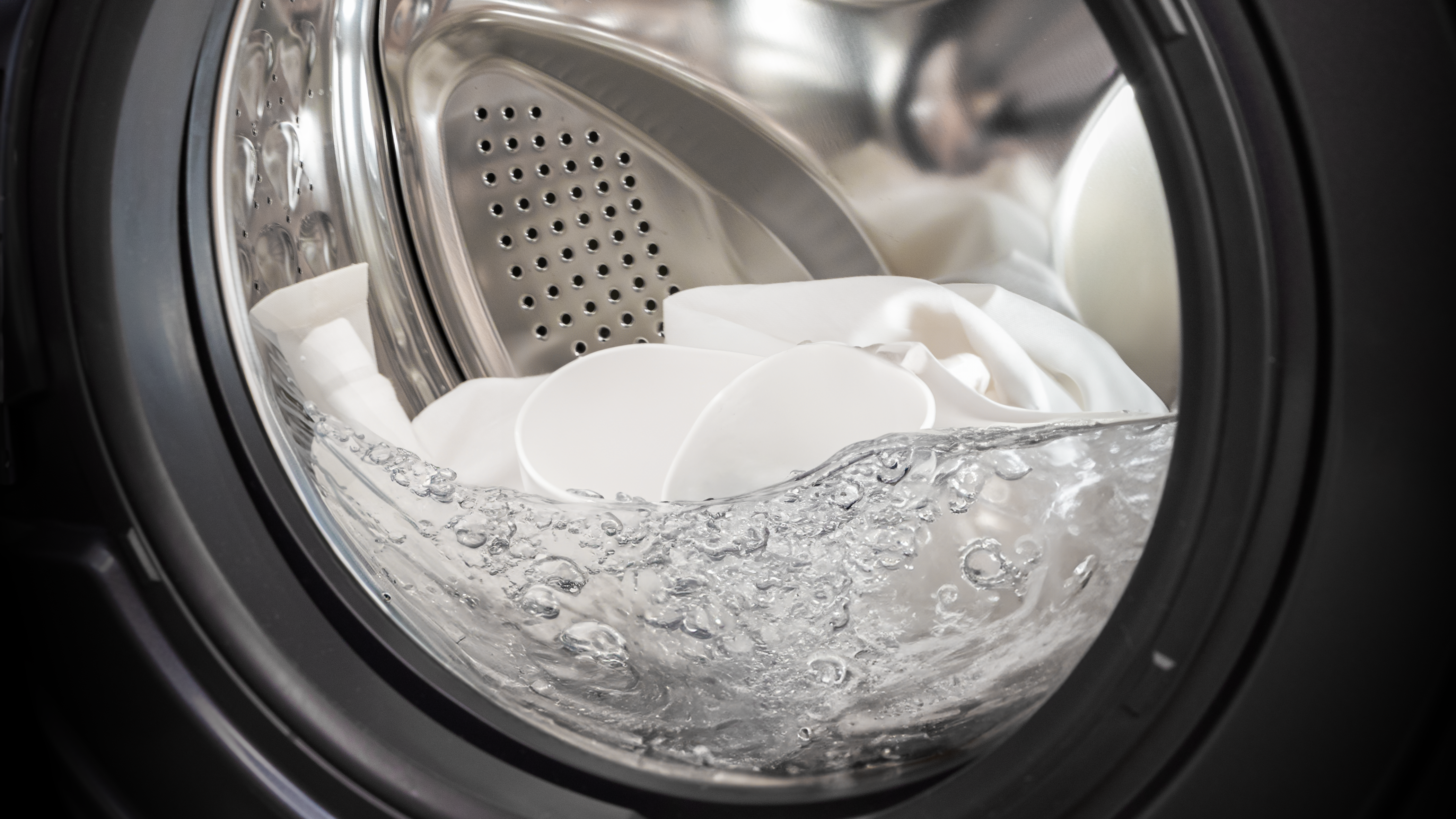 Un tambor de lavadora lleno de ropa blanca y agua, con burbujas visibles.