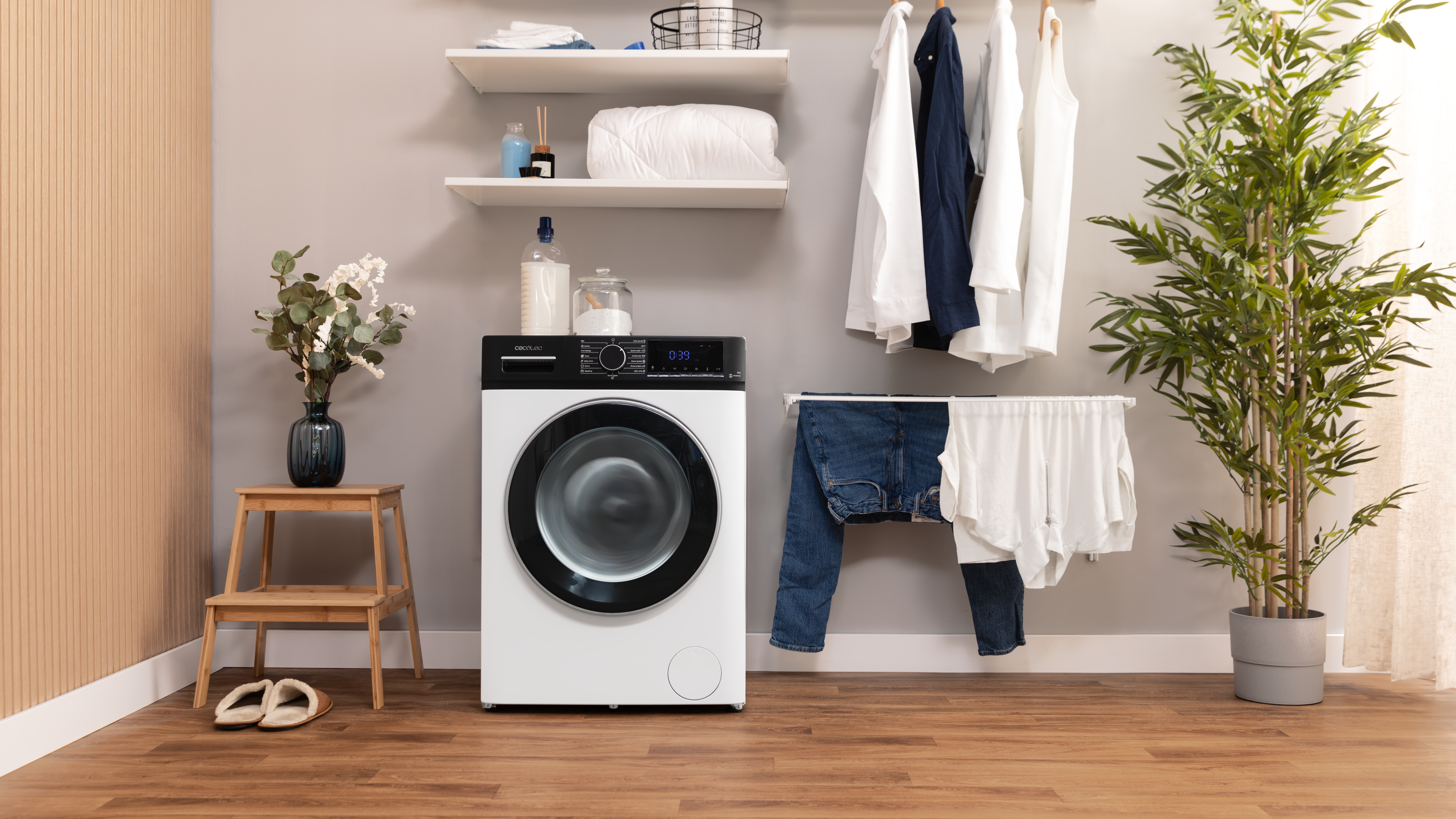 Cuarto de lavado con lavadora, ropa colgada, taburete de madera y artículos decorativos.