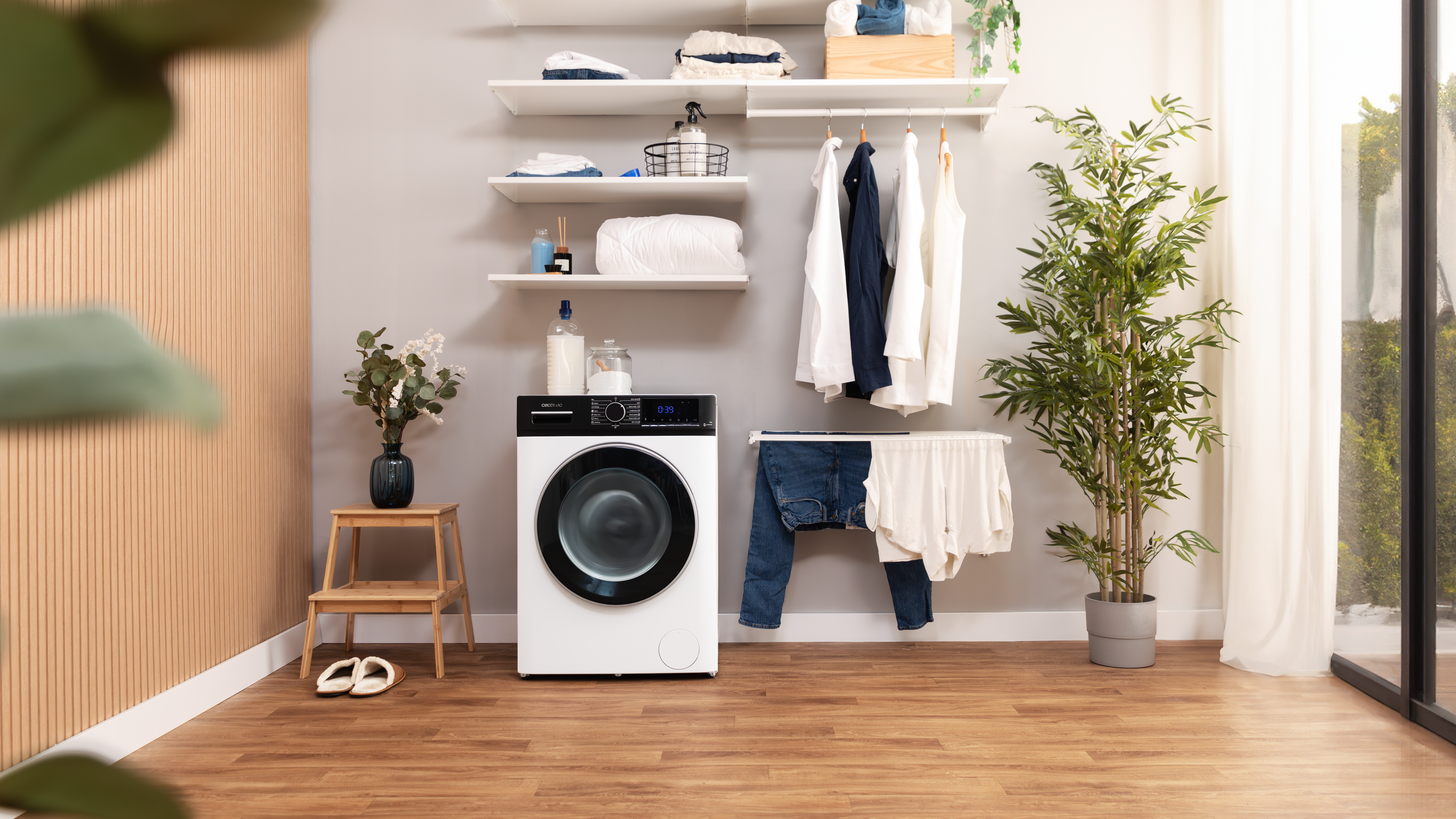Una lavadora en un cuarto de lavado con pisos de madera. Hay ropa en la rejilla y en los estantes.