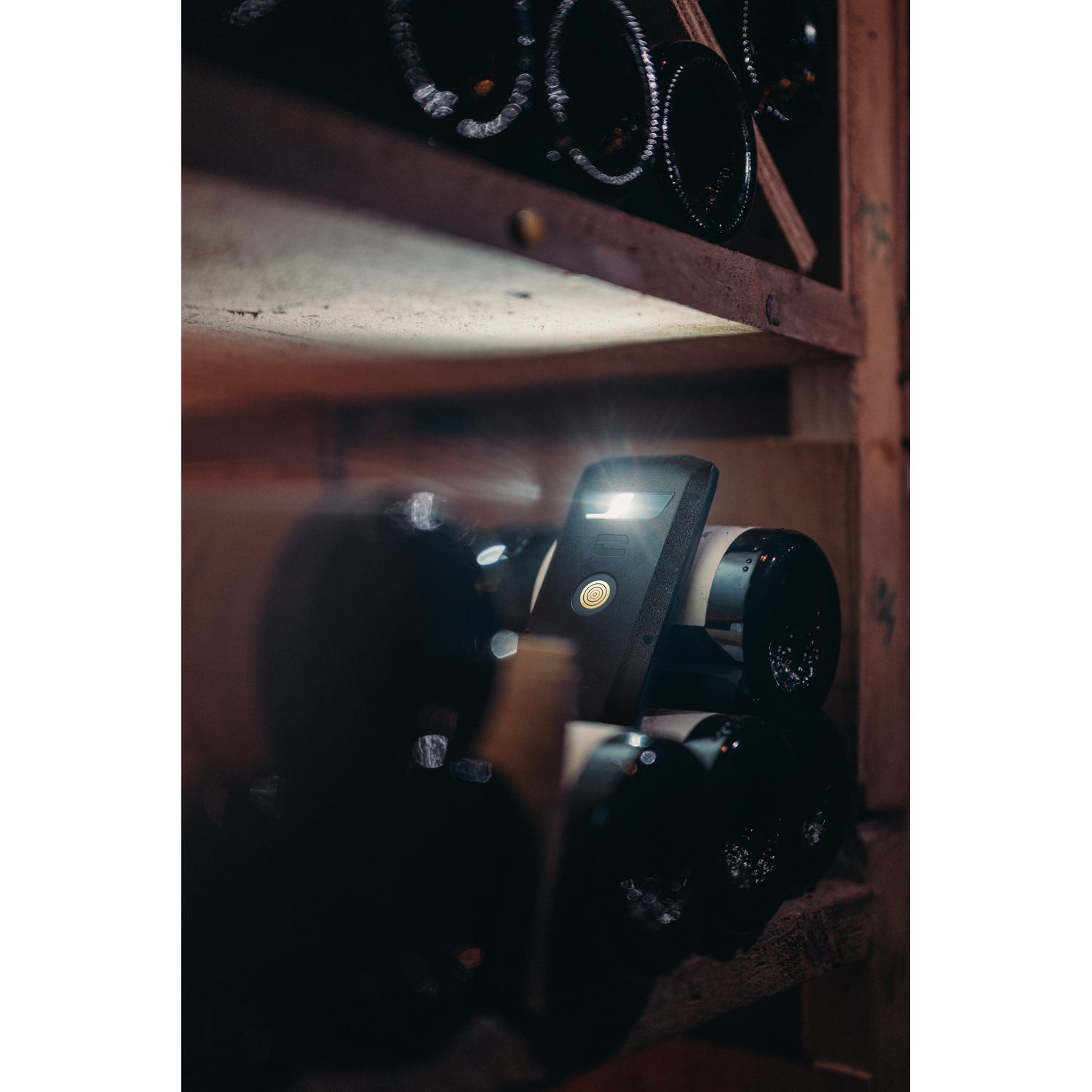 A black device is placed within a wine cellar, surrounded by wine bottles.