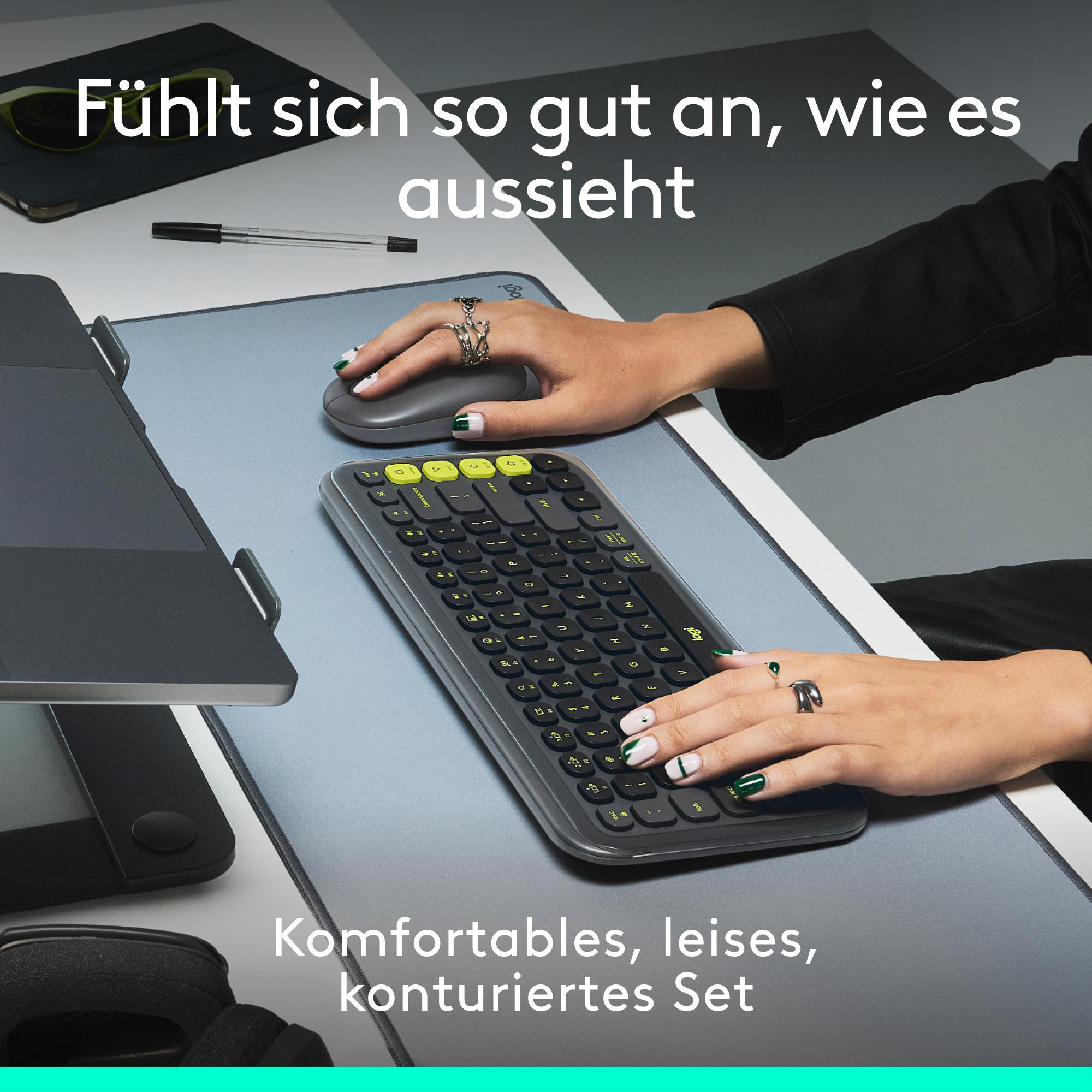 Hände benutzen eine Tastatur mit grünen Tasten und eine Maus auf einer grauen Schreibtischunterlage.