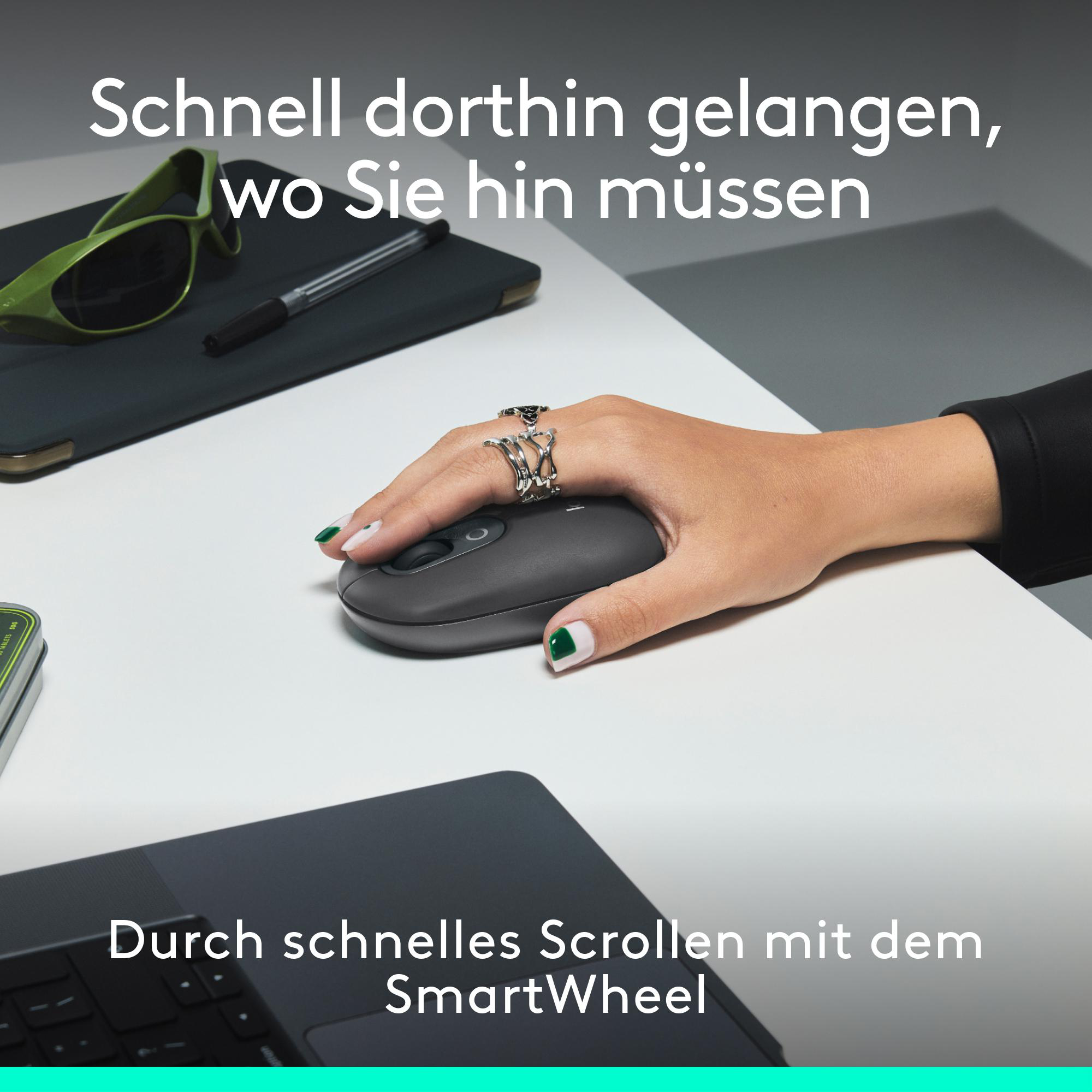 Eine Hand benutzt eine schwarze Maus auf einer weißen Oberfläche. Sonnenbrille und Stift liegen links.