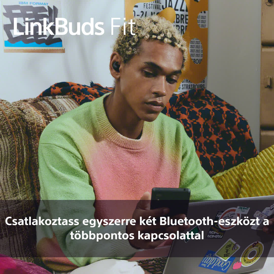 Egy személy LinkBuds Fit fülhallgatóval, telefont tartva. Háttérben laptop és poszterek.