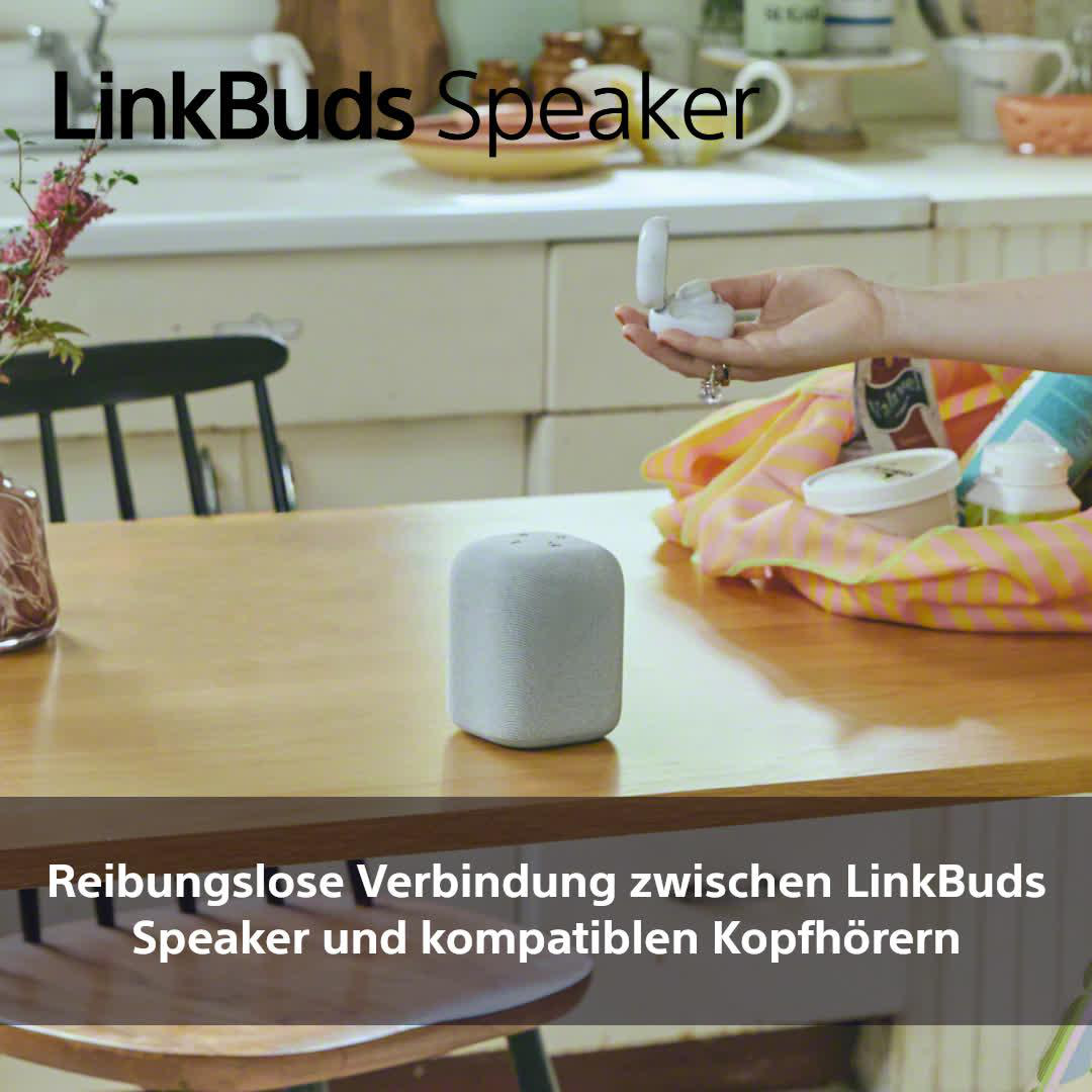 Grauer LinkBuds-Lautsprecher auf Holztisch. Person hält offene Ohrhörer-Hülle.