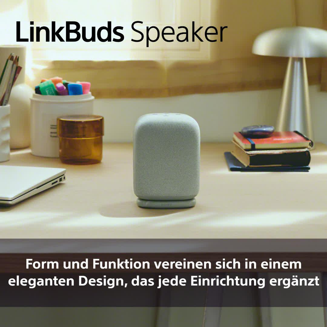 Grauer LinkBuds-Lautsprecher auf dem Schreibtisch. Lampe und Bücher im Hintergrund.