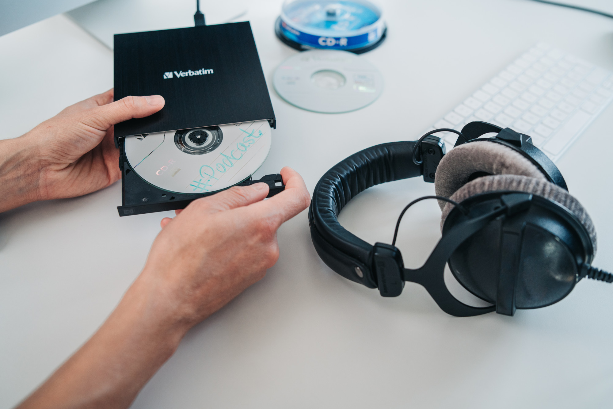 Ręce wkładające płytę CD do czarnej zewnętrznej nagrywarki CD ze słuchawkami.