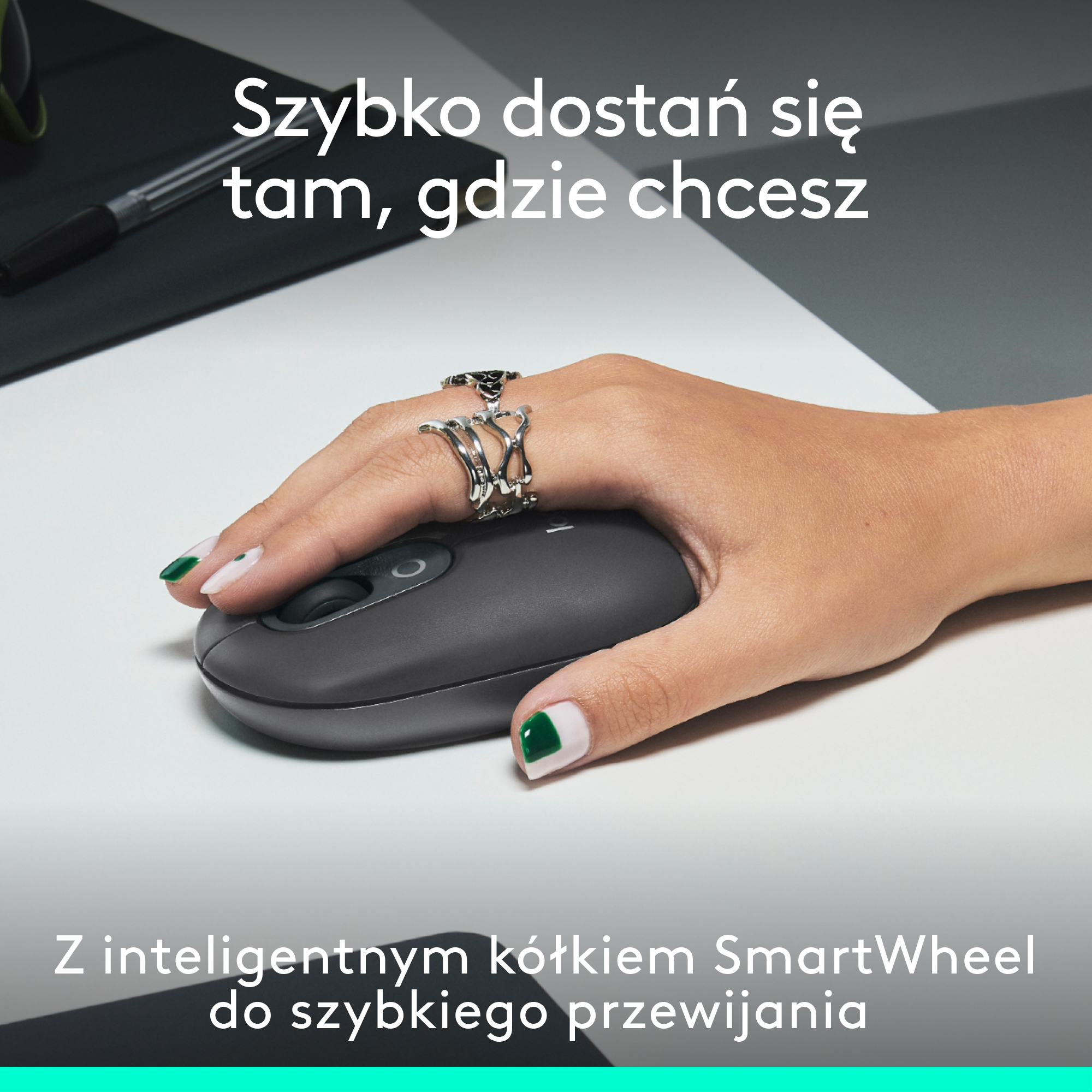 Dłoń z pierścionkami trzymająca szarą mysz komputerową na białej powierzchni. Na obrazie znajduje się tekst.
