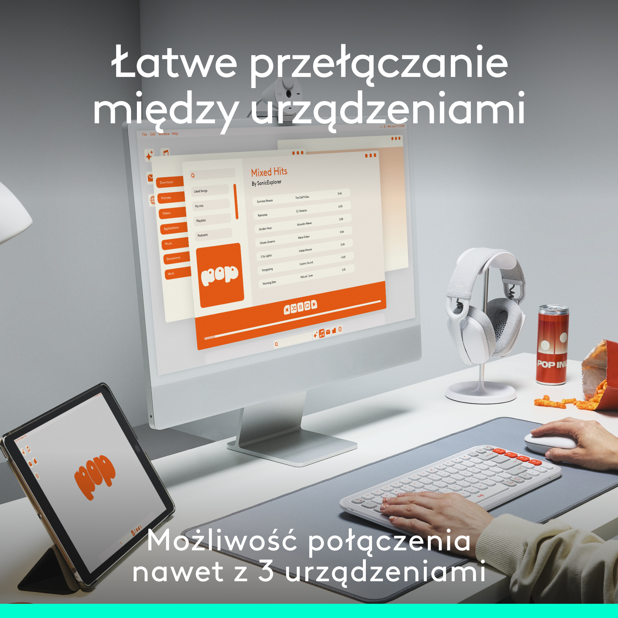 Osoba korzystająca z tabletu, klawiatury i słuchawek, z komputerem stacjonarnym w tle.