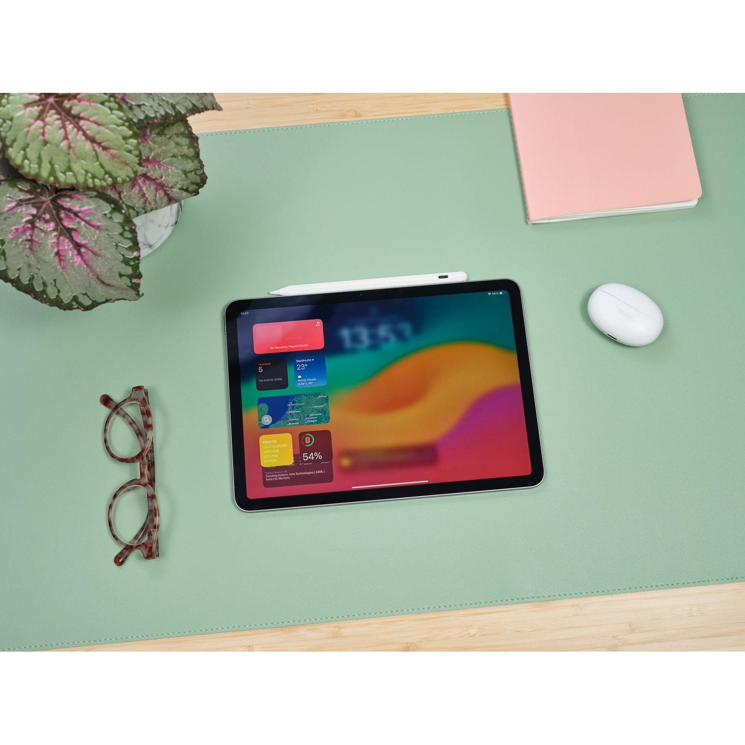 Un iPad con pennino, occhiali e un auricolare bianco su un tappetino verde.