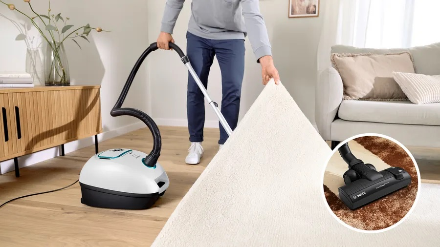 Osoba odkurzająca dywan nowoczesnym odkurzaczem w salonie.