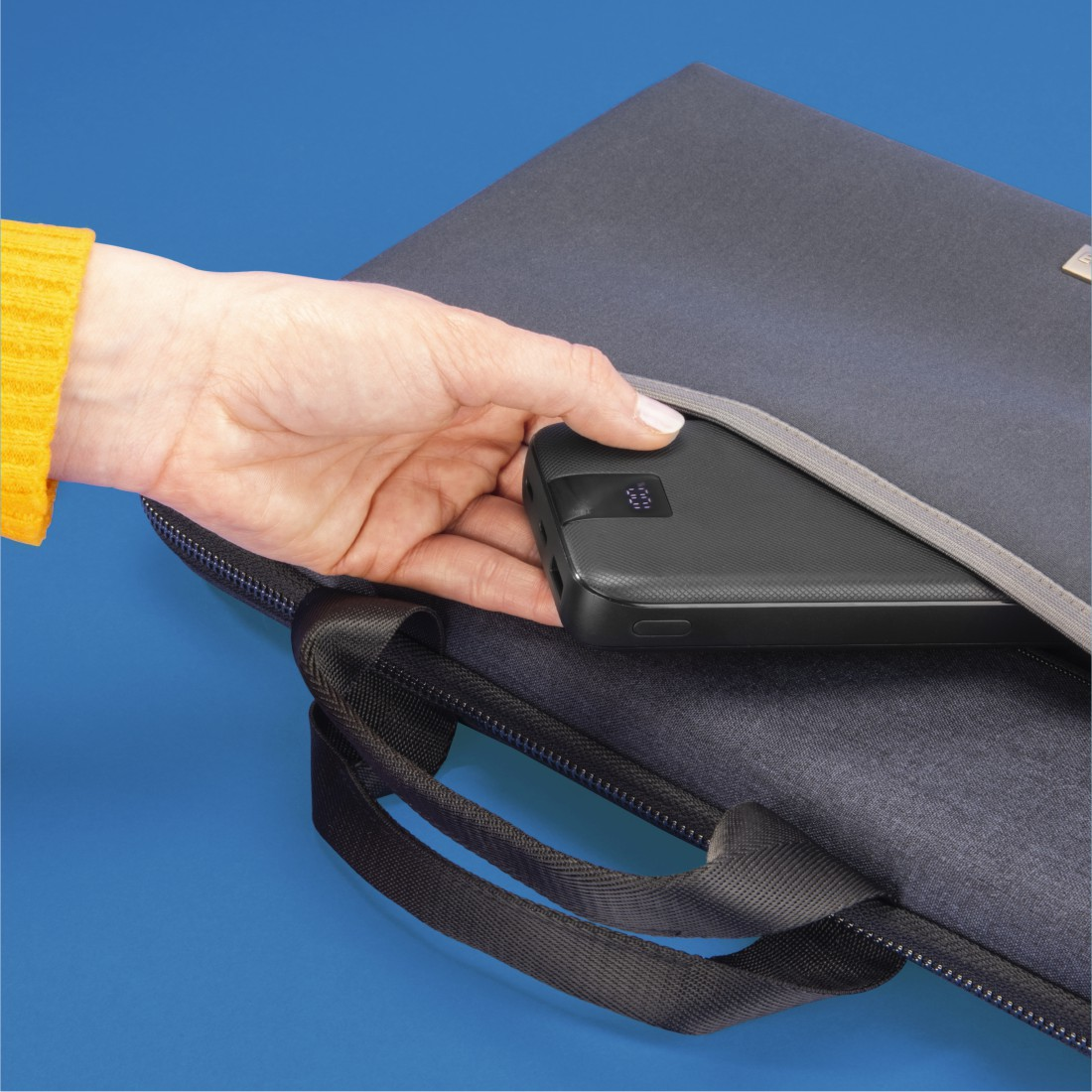 Eine Hand legt eine schwarze Powerbank in eine schwarze Tasche.