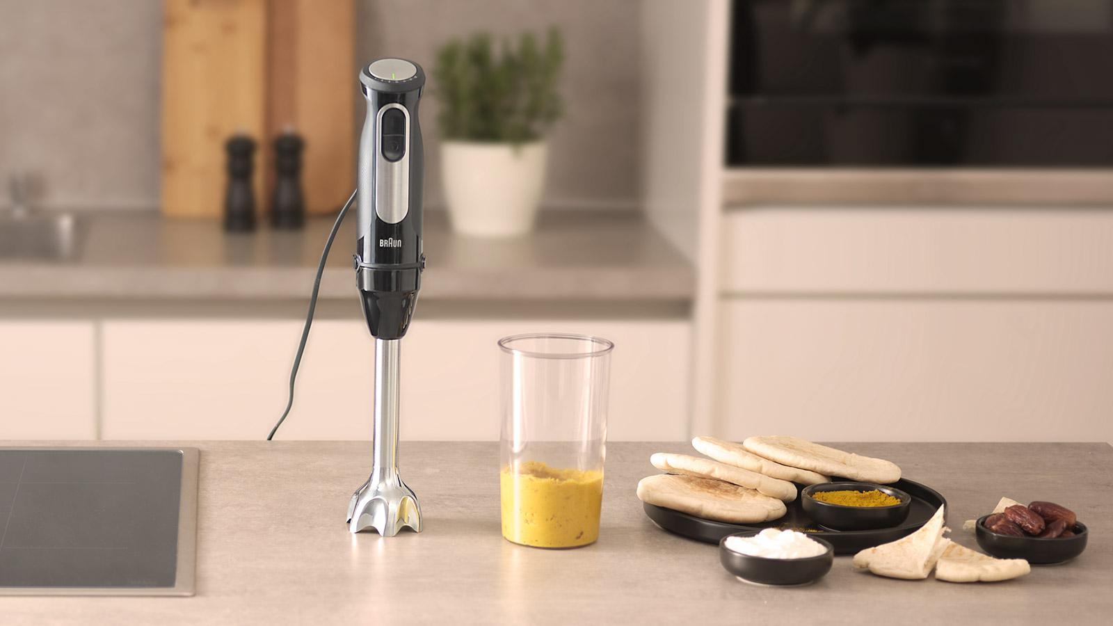 Ein Handmixer mit gelber Soße in einem Glas und Essen auf einem Tisch.