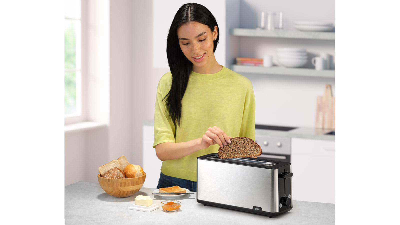 Eine Frau legt eine Brotscheibe in einen Toaster aus Edelstahl.