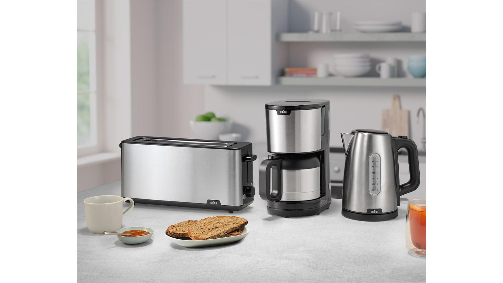 Ein Toaster, eine Kaffeemaschine und ein Wasserkocher auf einer Küchenarbeitsplatte. Alle sind Edelstahl.
