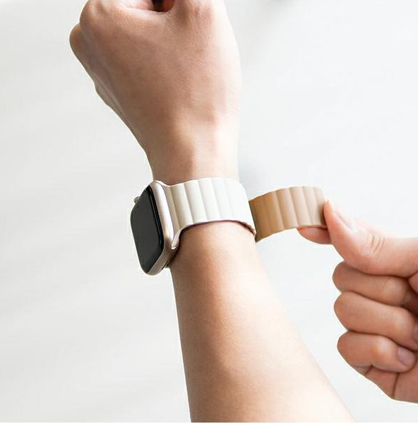 Ręka osoby mocująca beżowy pasek do złotego zegarka.