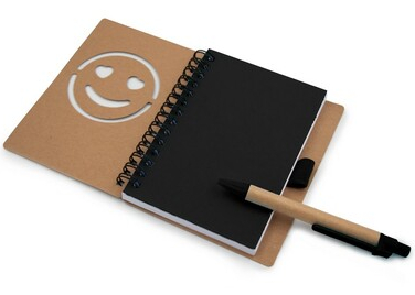 Notatnik z wyciętą buźką i długopisem. Notatnik jest otwarty.