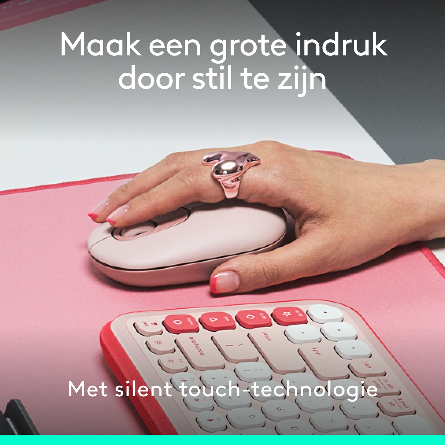 A woman's hand with a ring is using a pink mouse and keyboard on a pink surface.