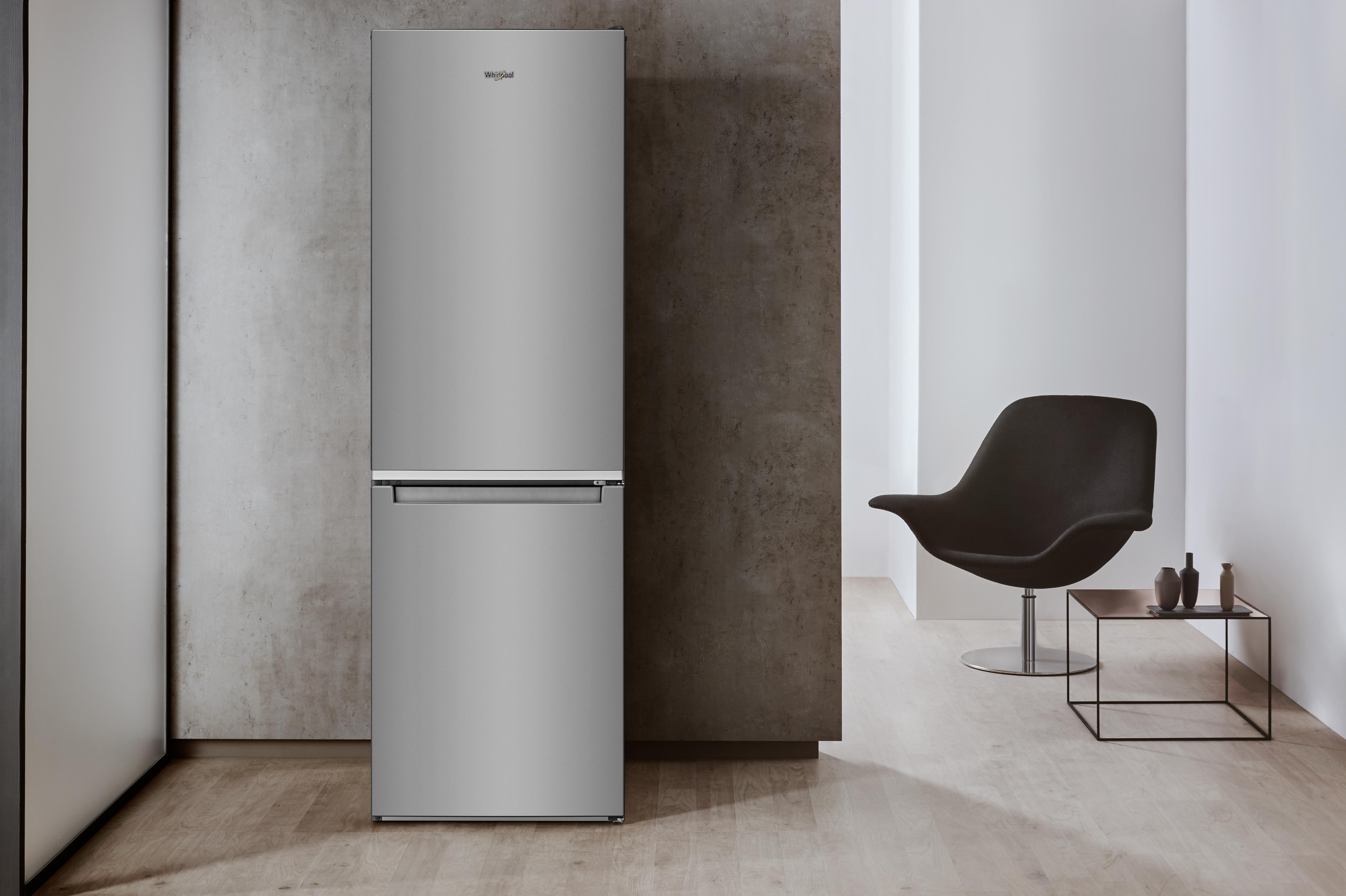 Srebrna lodówka stoi na tle betonowej ściany. Czarne krzesło i stół w tle.