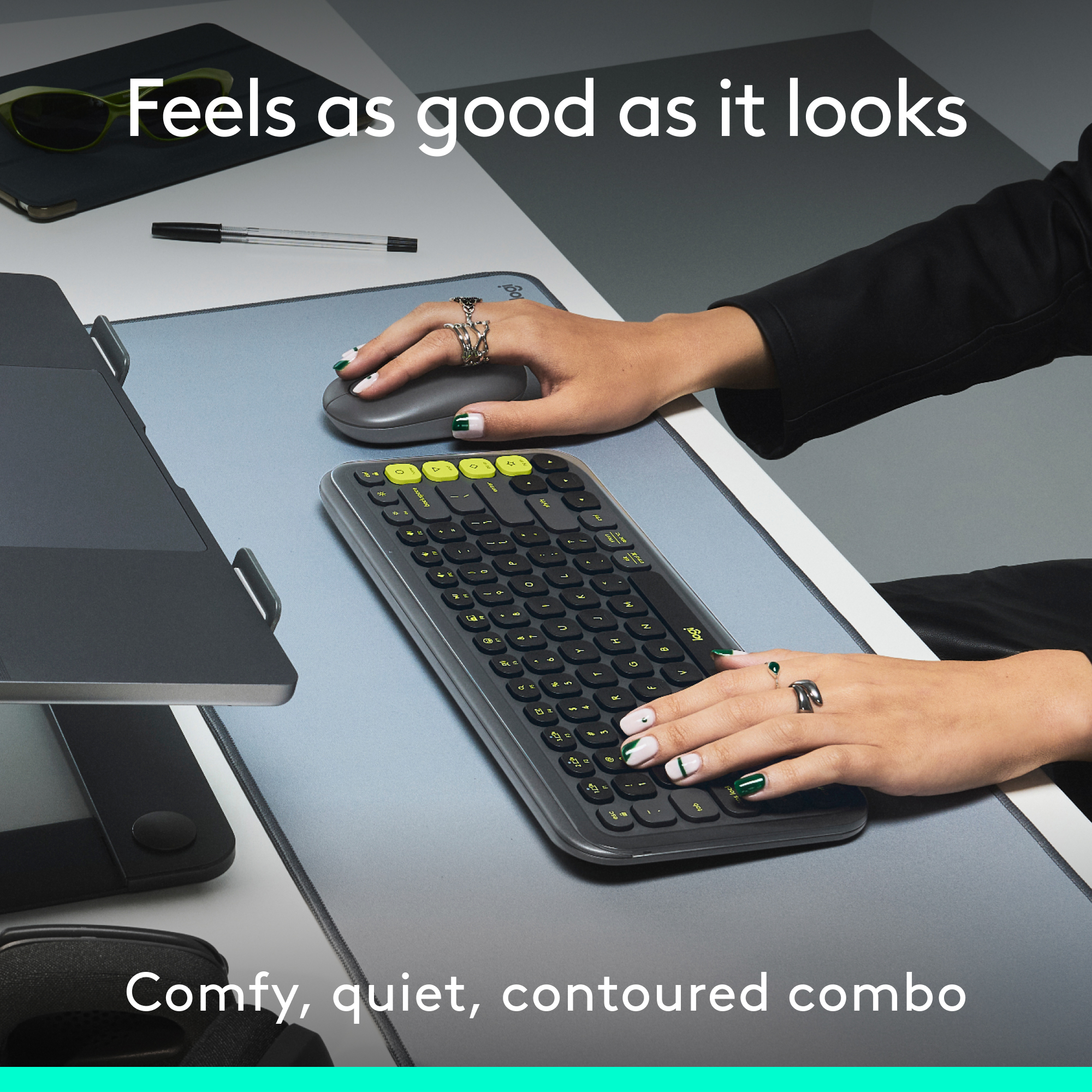 Mains d'une personne sur un clavier et une souris sur un tapis gris. Lunettes de soleil sur le tapis.