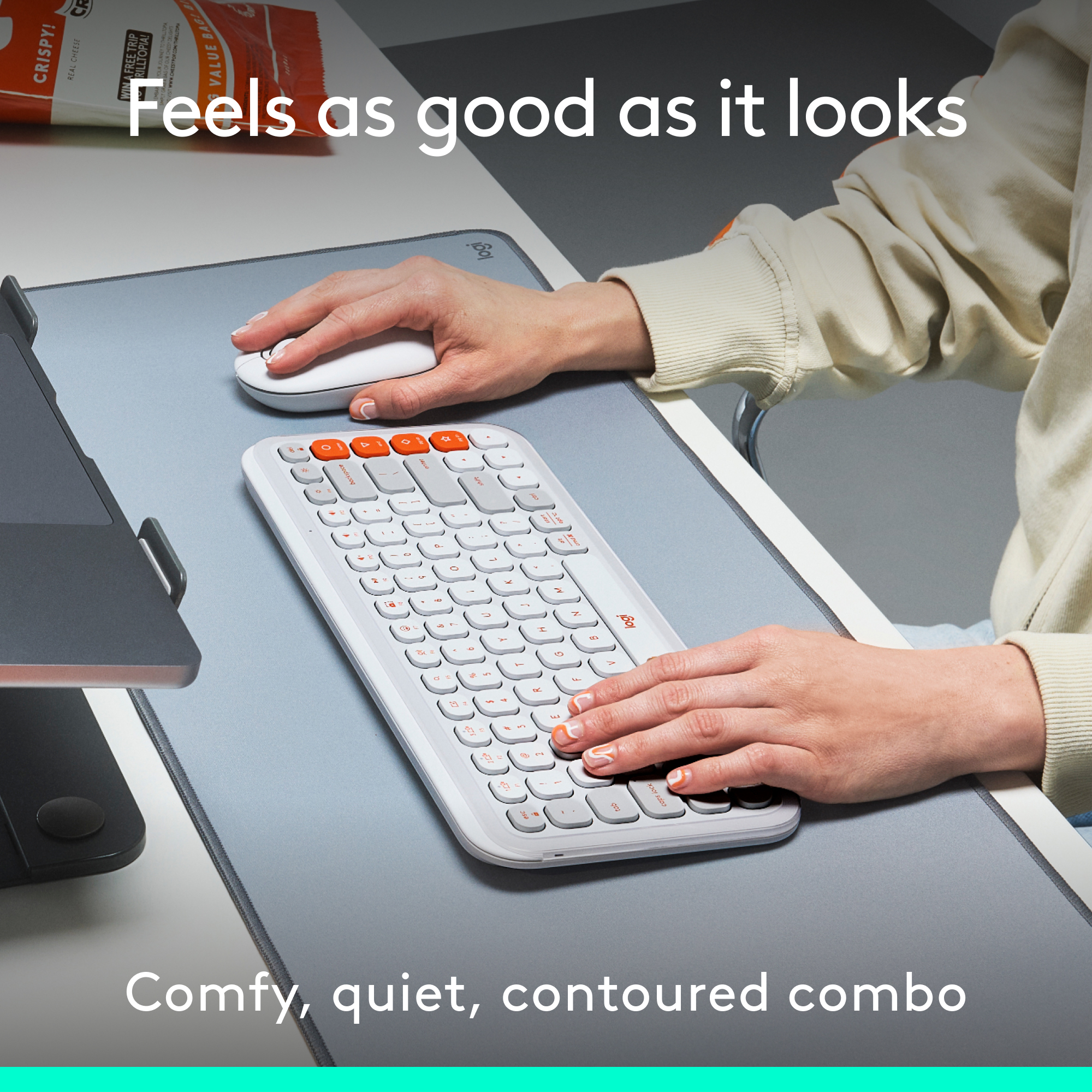 Une personne utilisant un clavier blanc et une souris sur un tapis de bureau gris, avec des collations sur le côté.