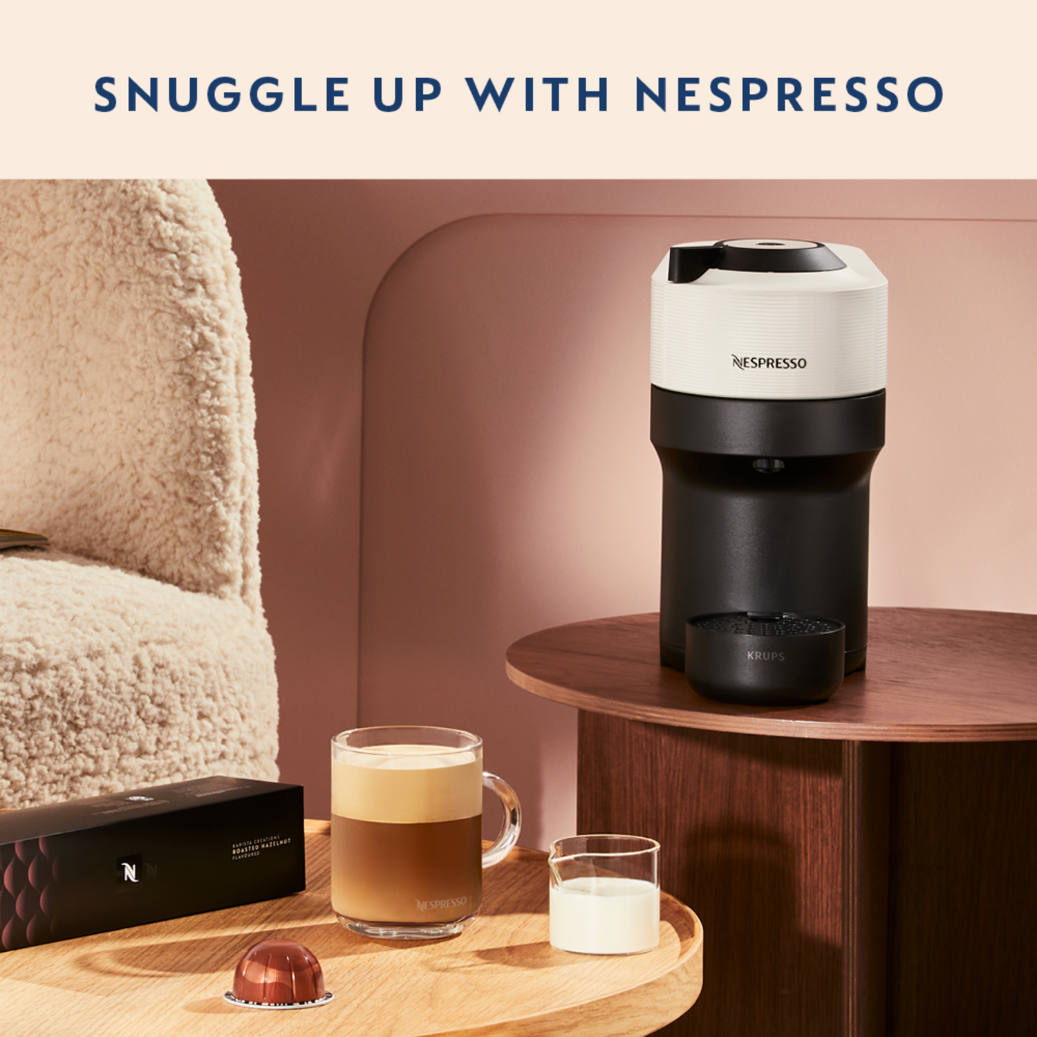 Nespresso machine, coffee cup, and milk jug on a wooden table.