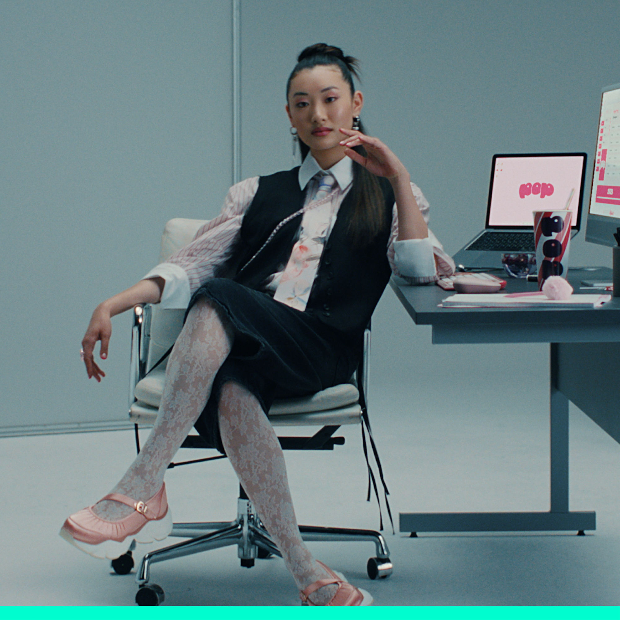 Femme assise à un bureau, ordinateur portable ouvert, en tenue de travail. Chaussures roses.