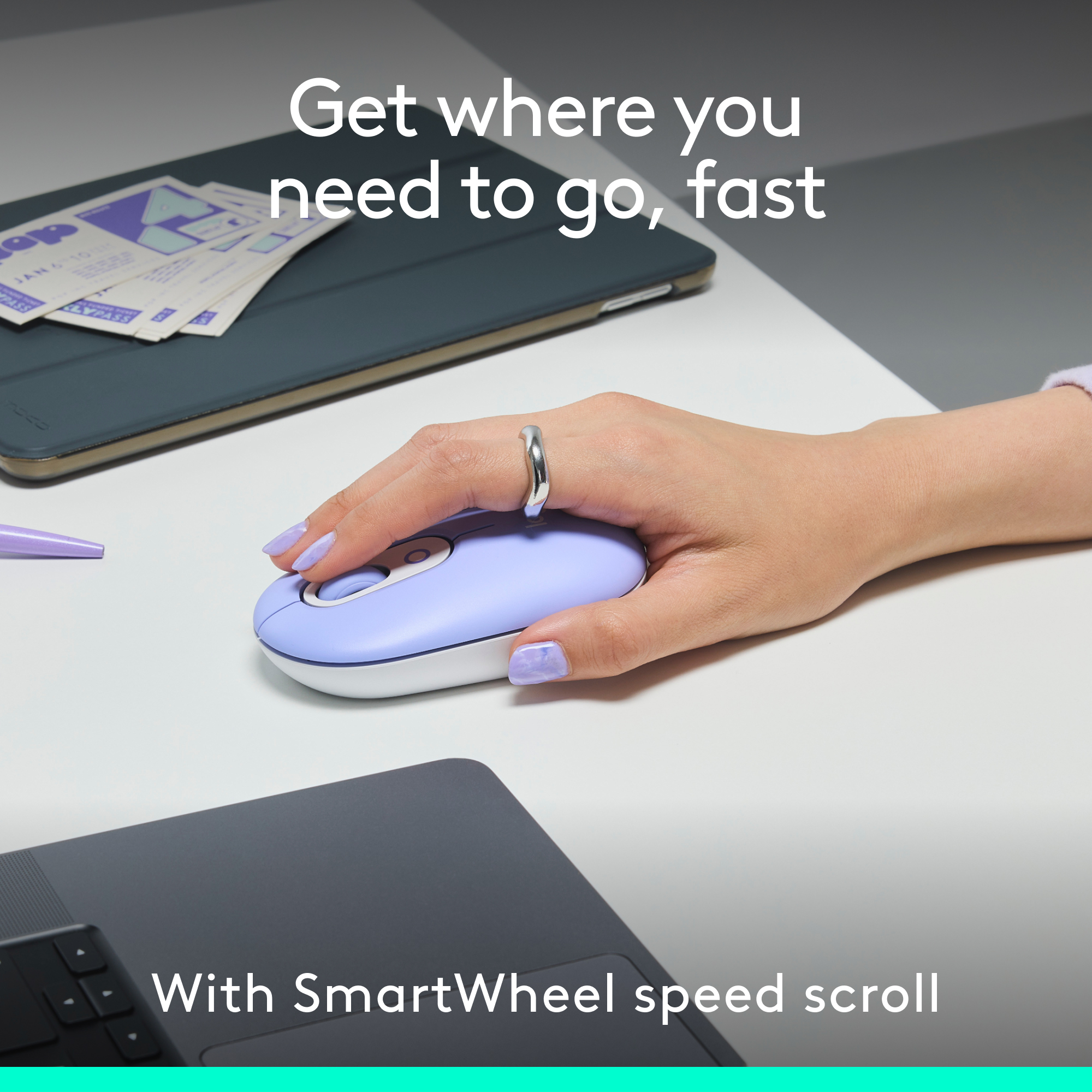 Une main utilise une souris bleu clair sur une surface blanche, avec une tablette et des papiers à proximité.