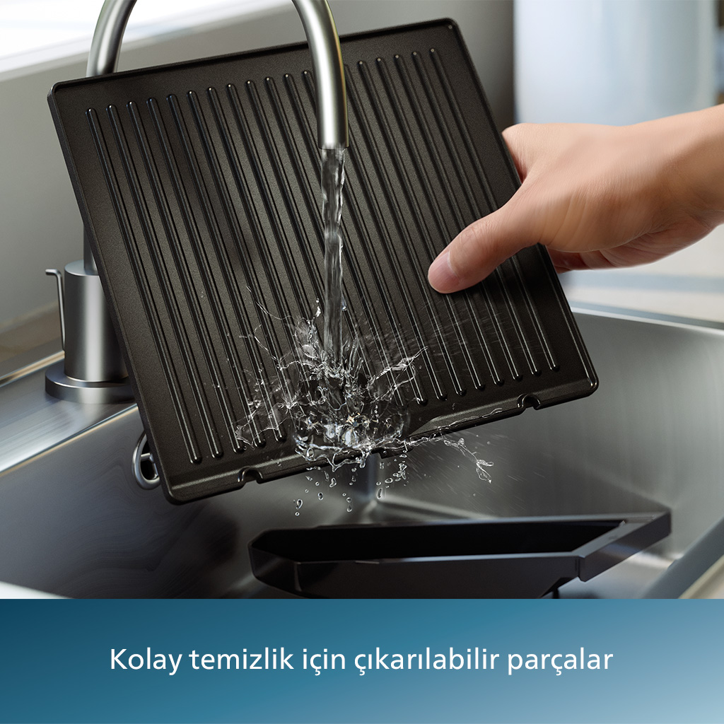El, ızgara plakasını musluk altında yıkıyor. Su siyah yüzeye sıçrıyor.