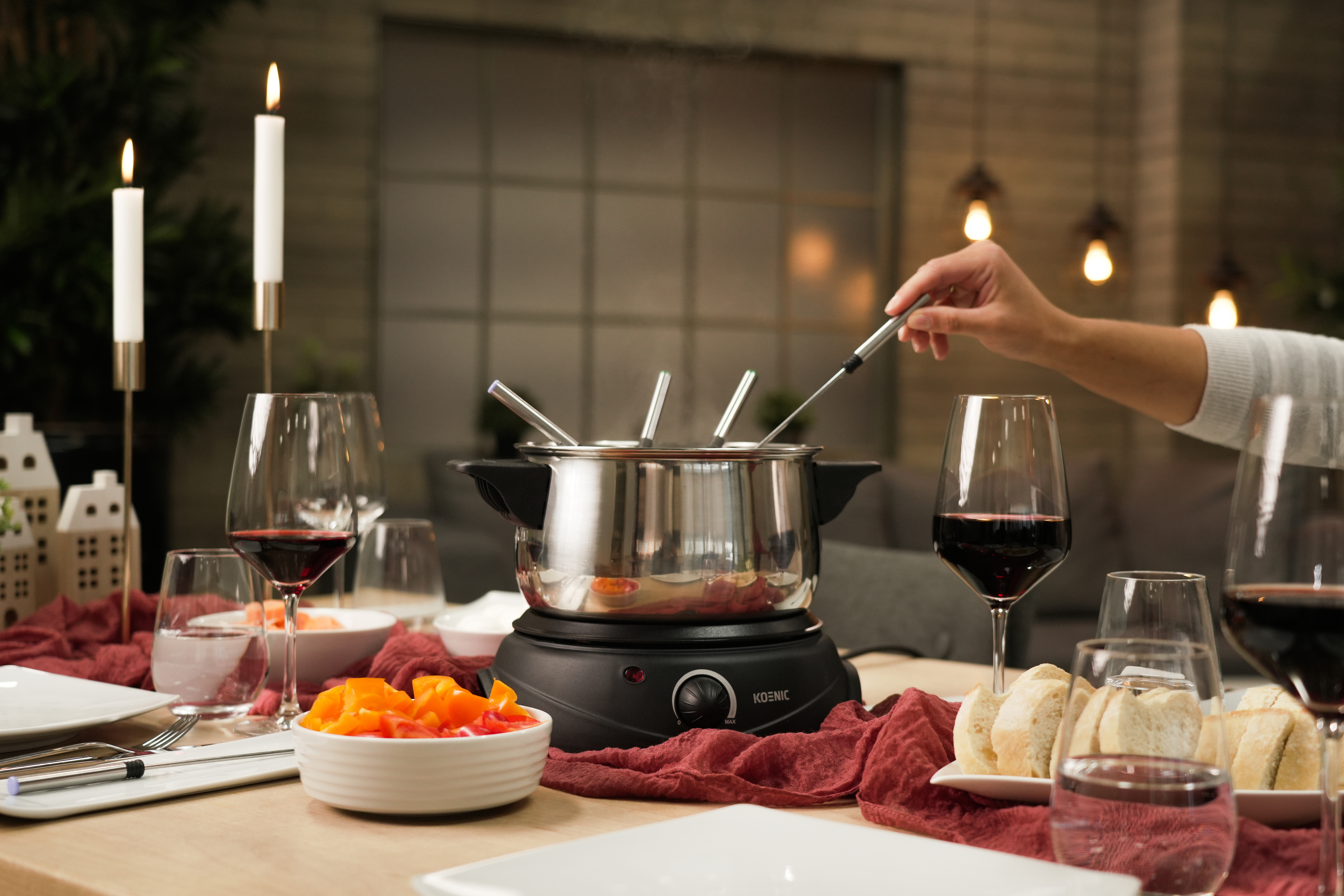 Fondue-Set mit Kerzen, Weingläsern und einer Hand, die Essen eintaucht. Holztisch.