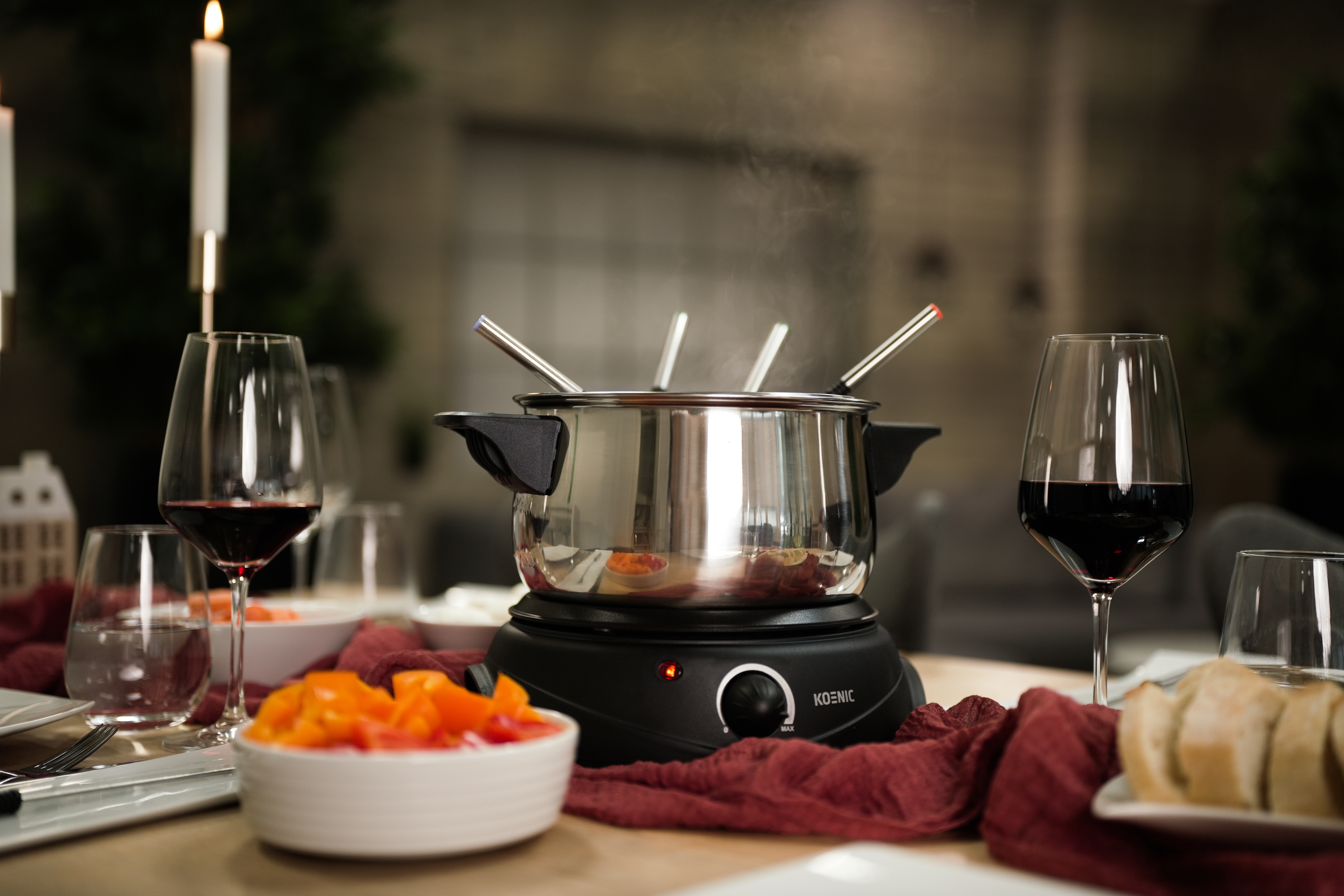 Fondue-Set auf einem für ein Essen gedeckten Tisch. Enthält Weingläser und Kerzen.