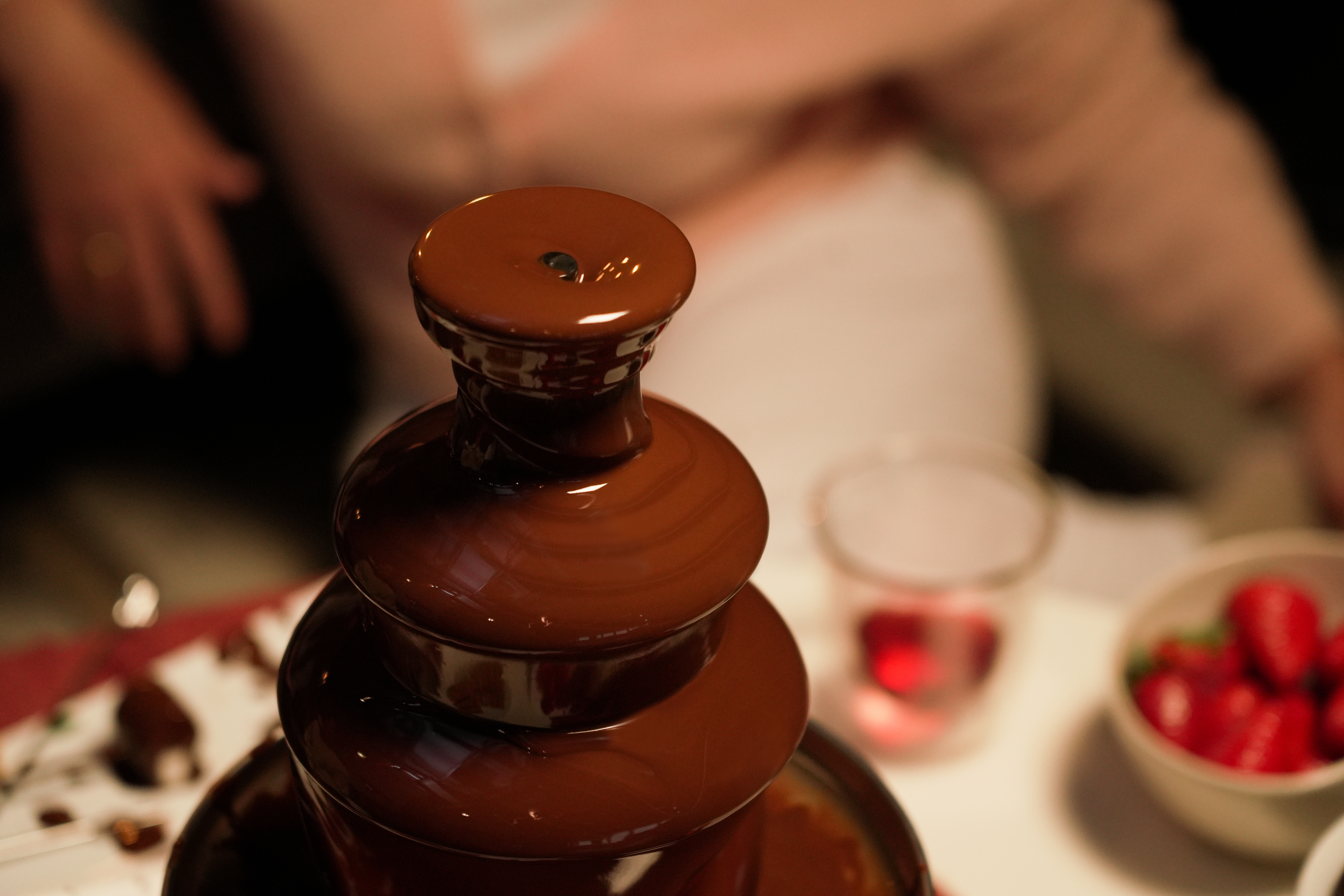 Schokoladenbrunnen mit fließender Schokolade, Erdbeeren und Glas auf weißer Oberfläche.