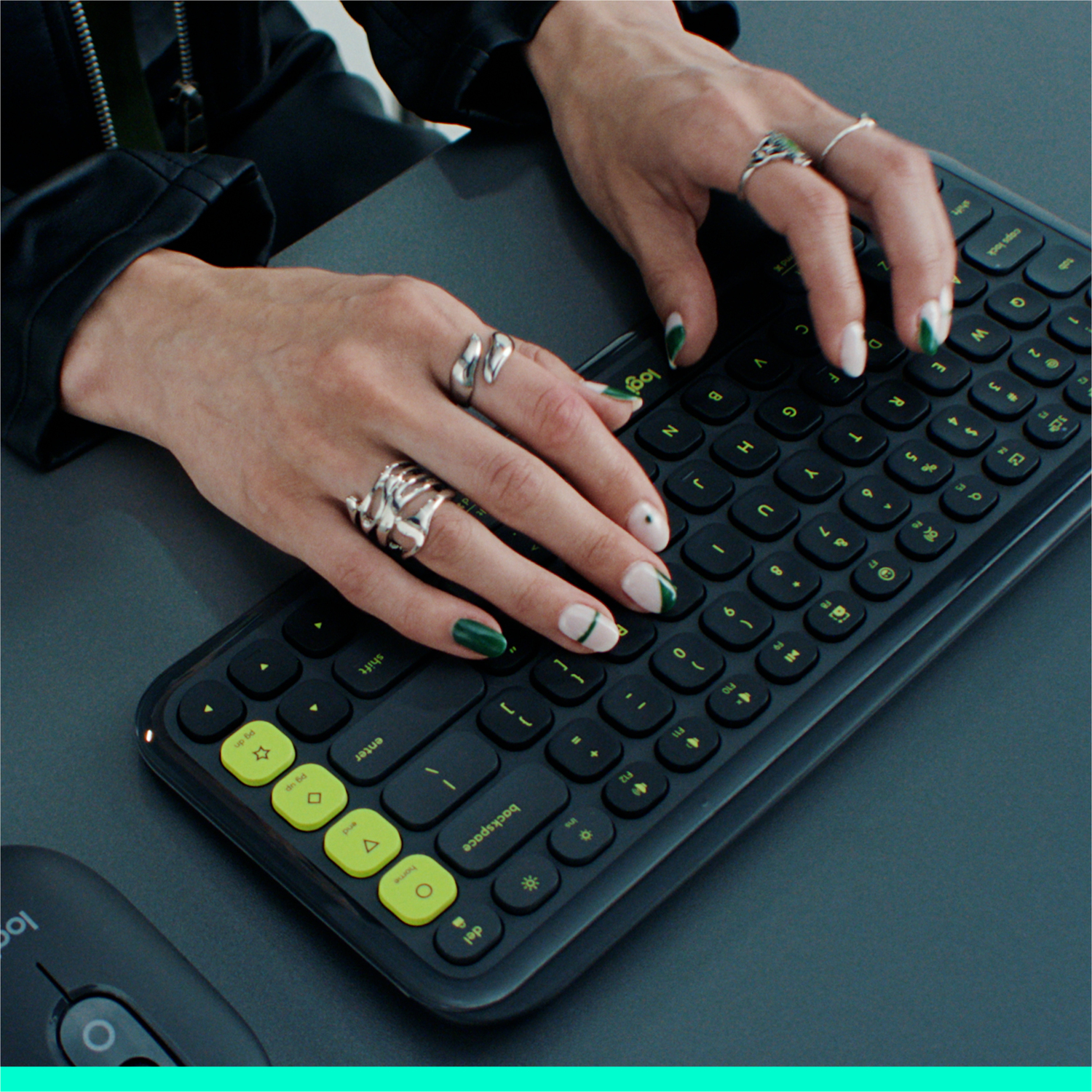 Handen typen op een zwart toetsenbord met groene toetsen, versierd met ringen. Nagels zijn groen en wit geschilderd.